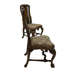 Pair of early 20th century Queen Anne design chairs, the cresting rail carved with scroll and central shell motif, shaped uprights and splat encased in cane work panels, shaped moulded seat frame with shell motif, floral needlework upholstered drop-in seat cushion, on shell carved cabriole supports with ball and claw feet, united by turned and shaped middle stretcher carved with acanthus leaf