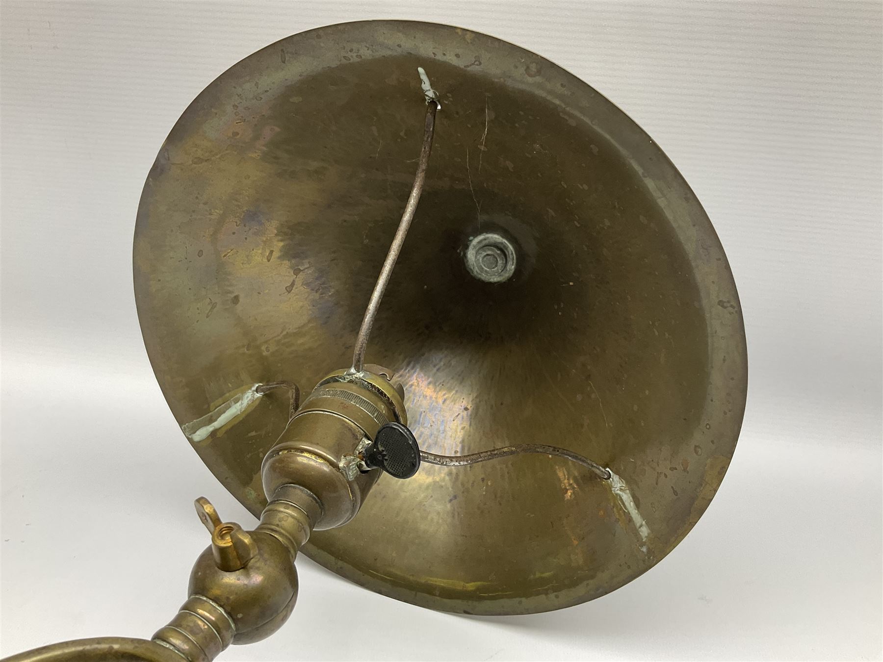 Arts & Crafts Jesson, Birkett & Co, brass table lamp or wall light, designed by Thomas Birkett, the tapering stem with adjustable ball pivot supporting a conical shade with tapering final with ball terminal, upon a circular domed base pierced for wall mounting, shade positioned upright overall H57cm

Often misattributed to Arthur Stansfield Dixon for Birmingham Guild of Handicraft, this particular lamp was designed by Thomas Birkett.
In the late 1890's Birkett worked as a metalwork at the Birmingham Guild, before later joining the Faulkner Bronze Company which went on to become Jesson, Birkett & Co in 1904. The lamp features in lighting catalogues from the firm under the model no E490.

