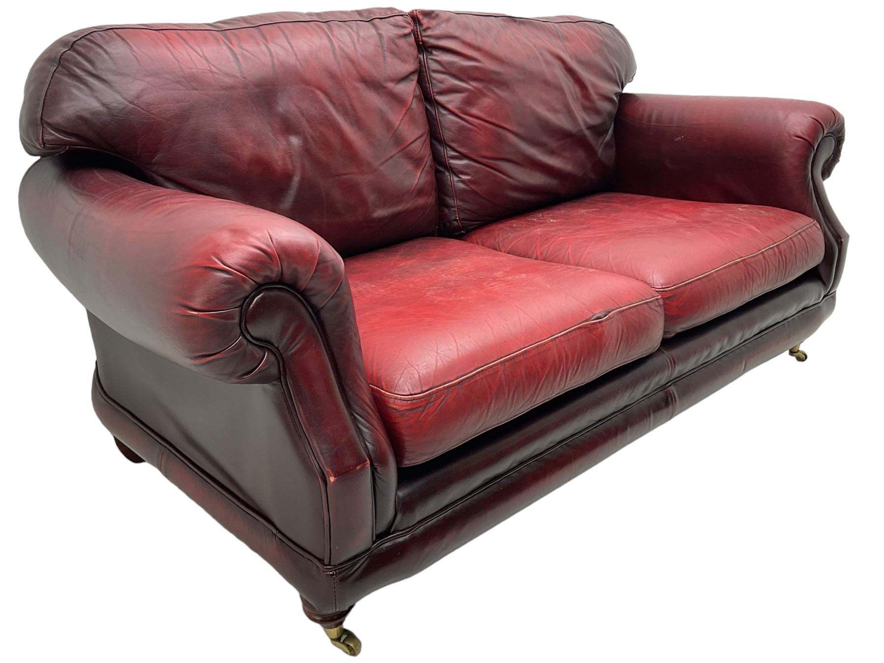 Thomas Lloyd - three-piece lounge suite, comprising of traditional shape two seat sofa (W190cm H80cm) and a pair of wingback armchairs (W100cm H91cm), each with rolled arms over turned supports with brass castors, upholstered in oxblood red leather
