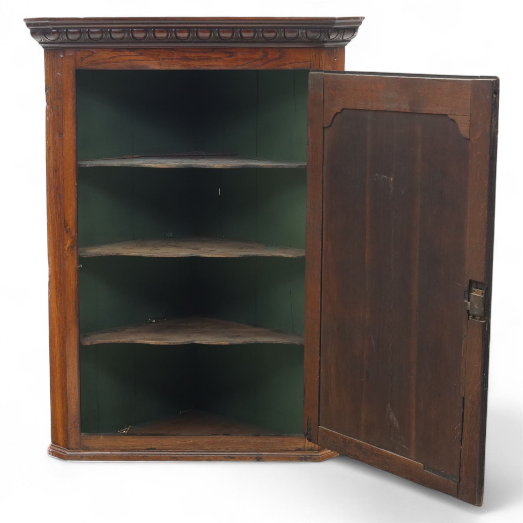 19th century oak wall hanging corner cupboard, moulded cornice above a panelled door enclosing shaped interior shelves, finished in green paint to the backboards