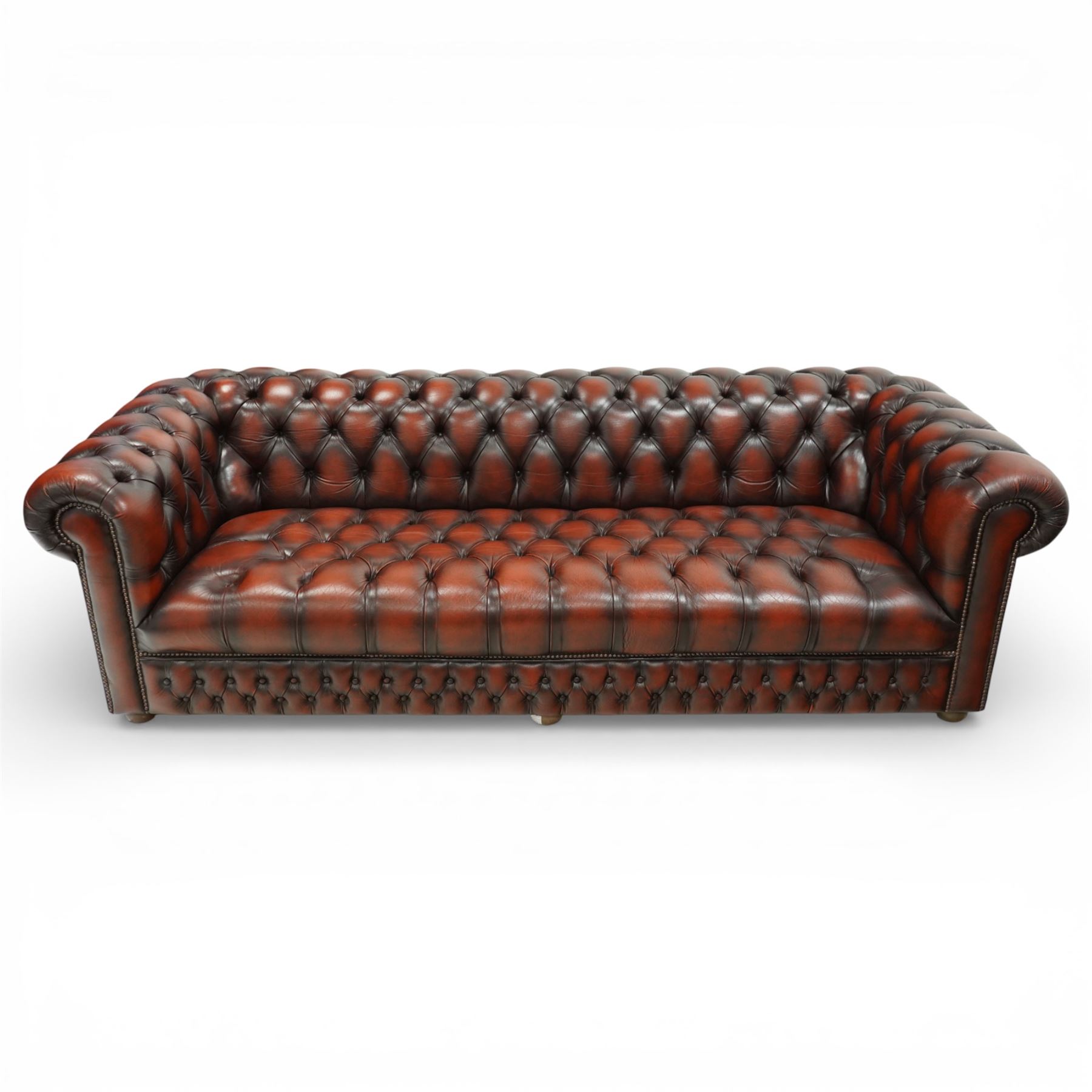 Late 20th century four seat Chesterfield sofa, upholstered in deep buttoned brown leather, with rolled arms, buttoned back and seat, studded detailing and squat feet