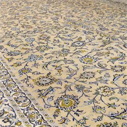 Central Persian Kashan hand-knotted carpet, pale ivory ground, decorated with an all-over scrolling floral design of palmettes rosettes, and leafy vine work enclosed by a wide floral border and multiple guard borders in tones of soft blues, sage green, muted gold, and ivory, with cotton fringe ends