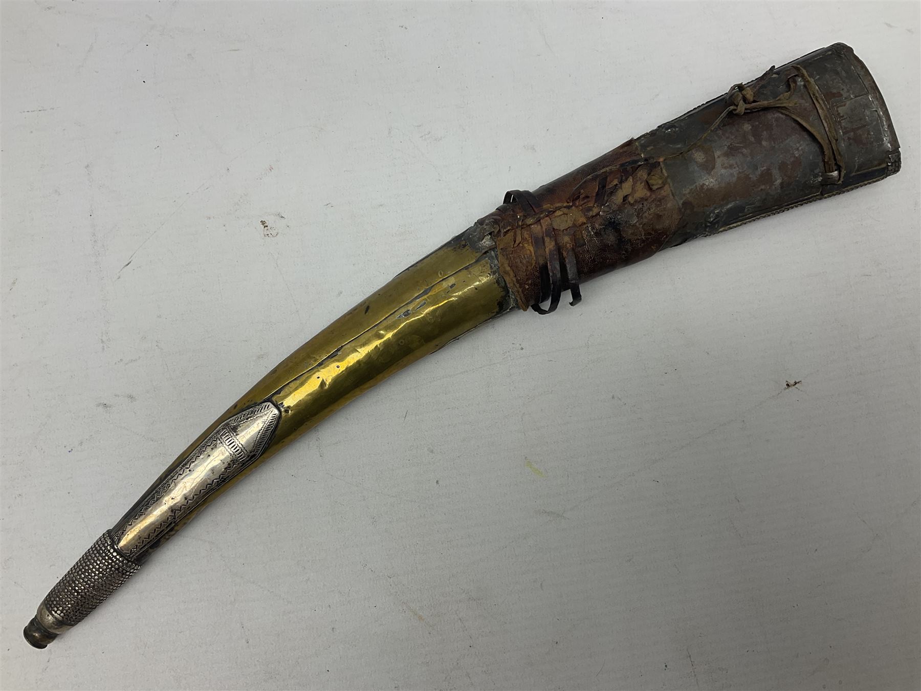 Late 19th/20th century Middle Eastern jambiya dagger the 36cm broad curved double edged steel blade with traces of script, horn and copper backed waisted white metal hilt with three roundel buttons; in ornate white metal and leather mounted brass and steel scabbard L60.5cm overall
