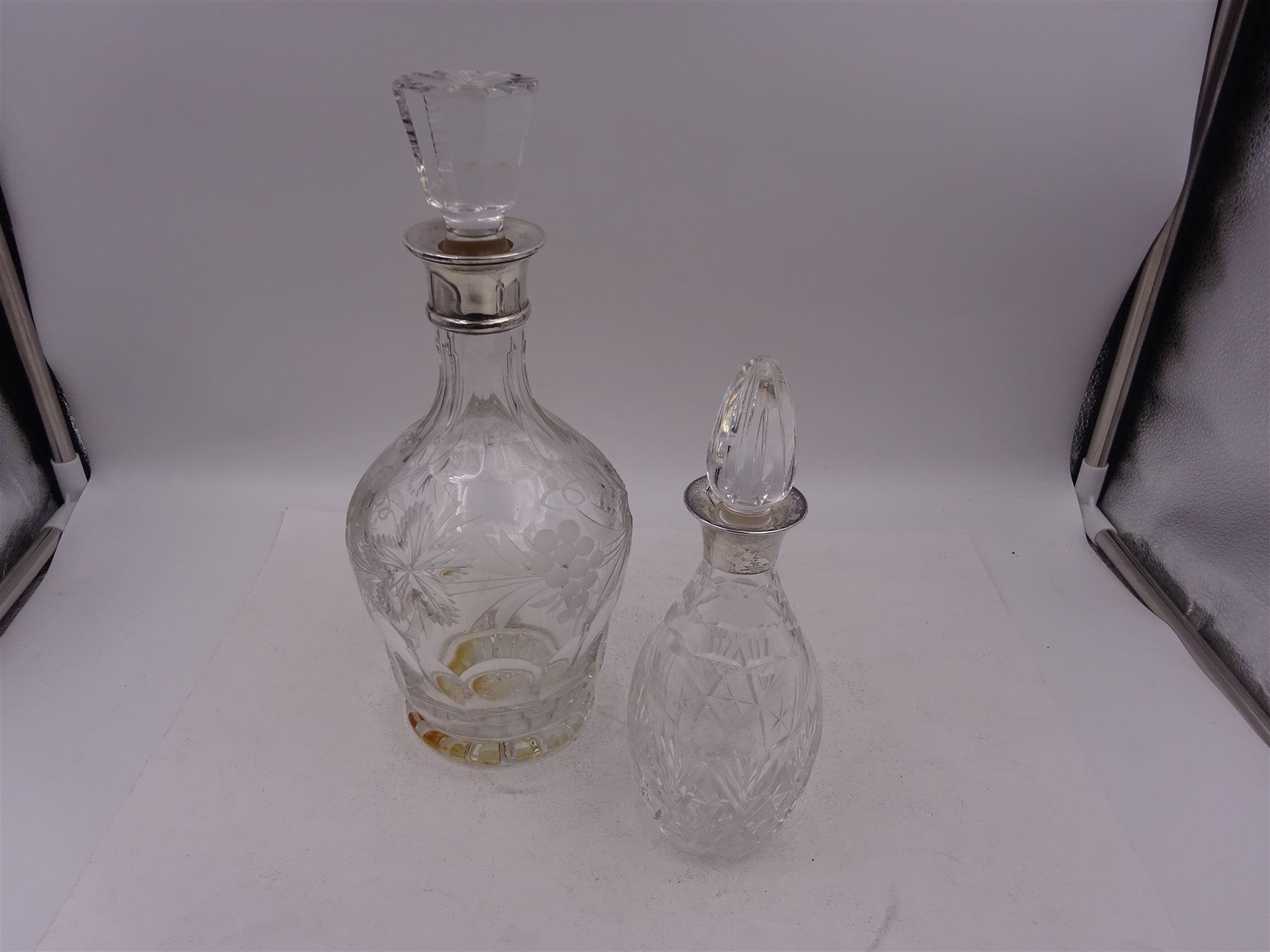 Two modern silver mounted decanters, the first example with etched and cut fruiting vine decoration to glass body, with faceted stopper, hallmarked C J Vander Ltd, Birmingham 1980, the second smaller example, with oval cut decoration and flambe type stopper, hallmarked S J Rose & Son, Birmingham 1985, tallest H28.5cm