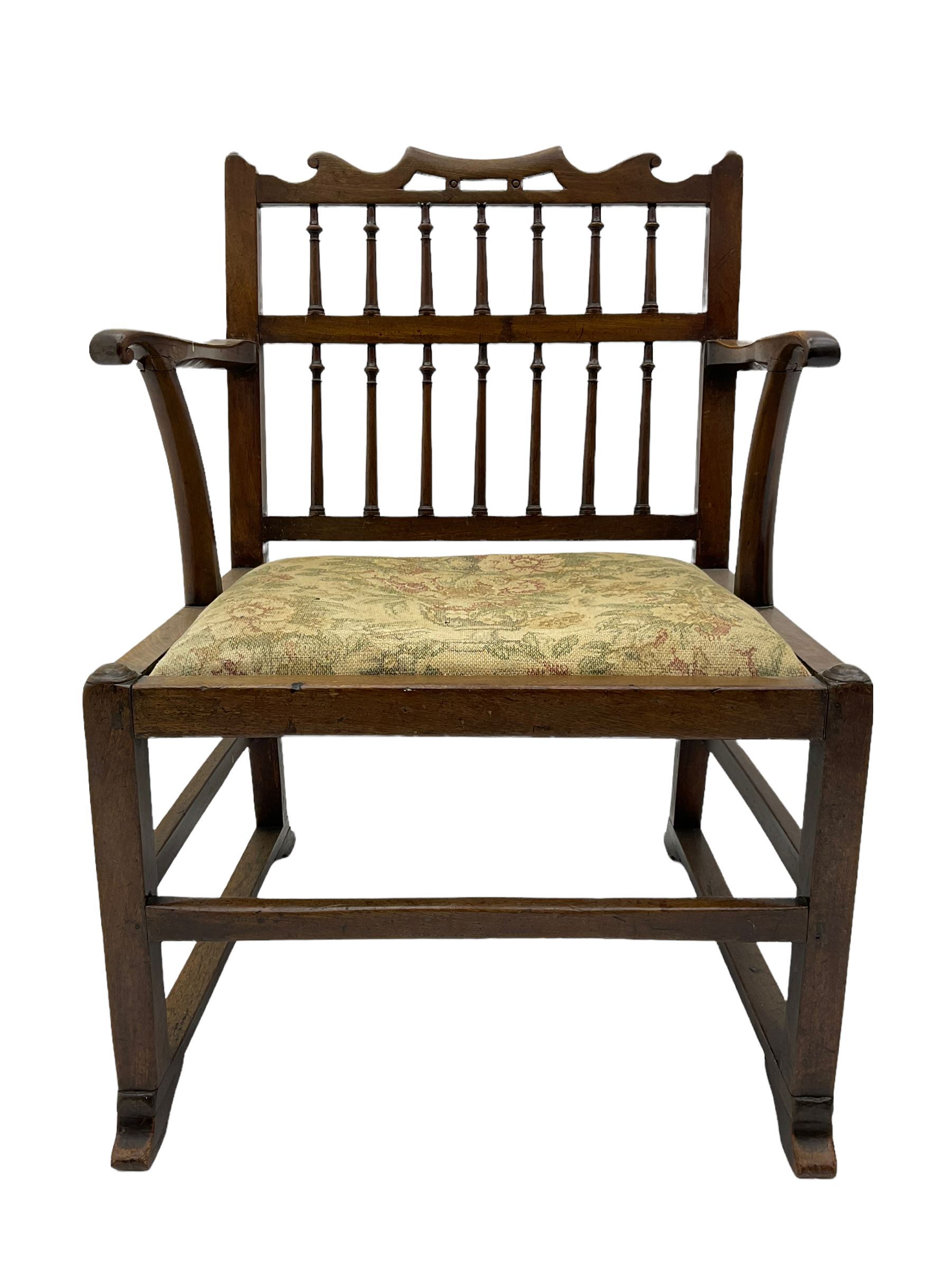 Late 18th century walnut 'Drunkard's' chair, the shaped cresting rail over spindle back, wide set seat with upholstered drop in cushion, shaped arms with scroll carved terminals, sledge supports with bracket feet joined by plain stretchers 