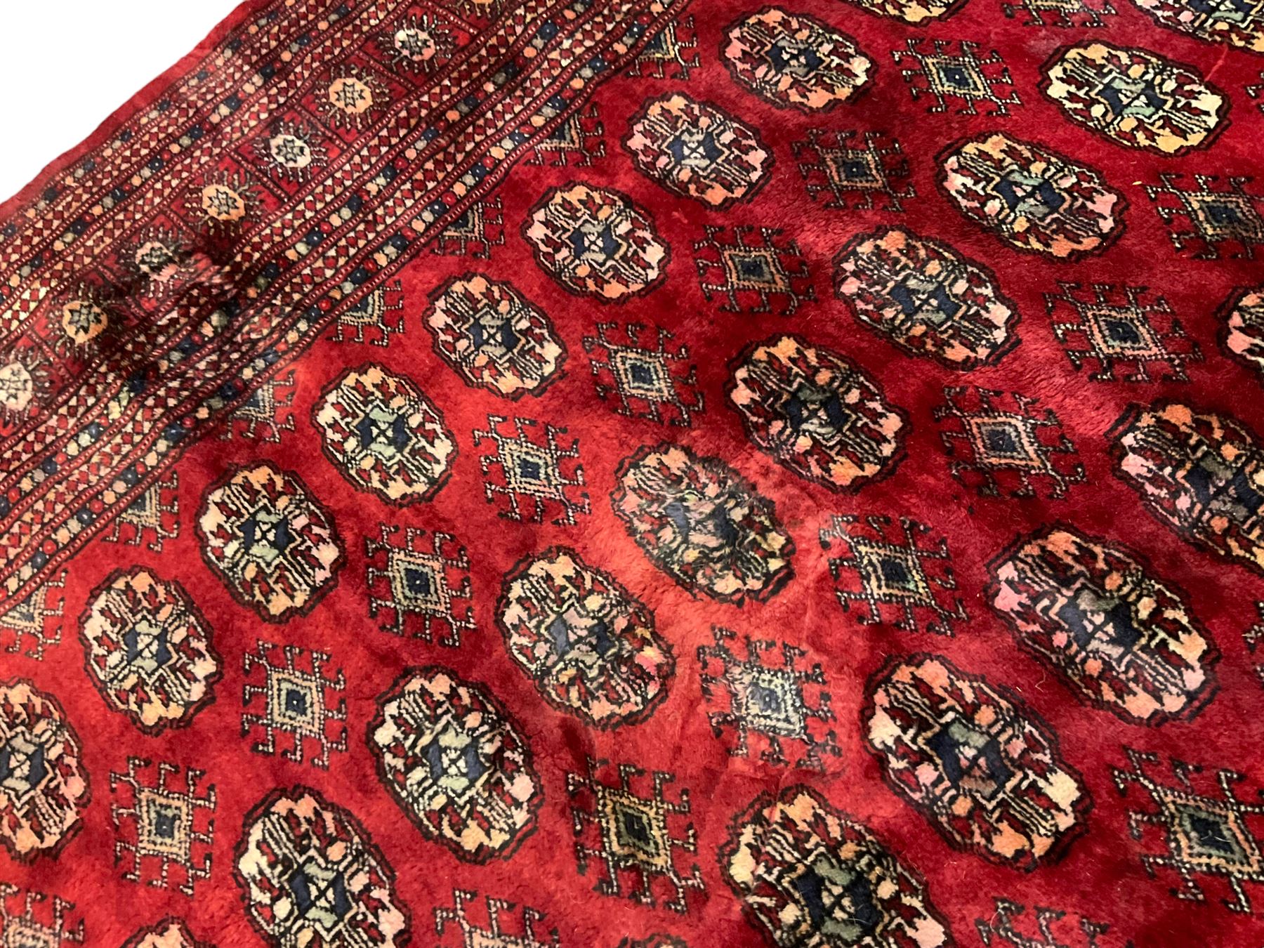 Pakistani Bokhara red ground rug, the field decorated with repeating Gul motifs and lozenges, the multi-band border with stylised plant motifs with dark indigo outlines