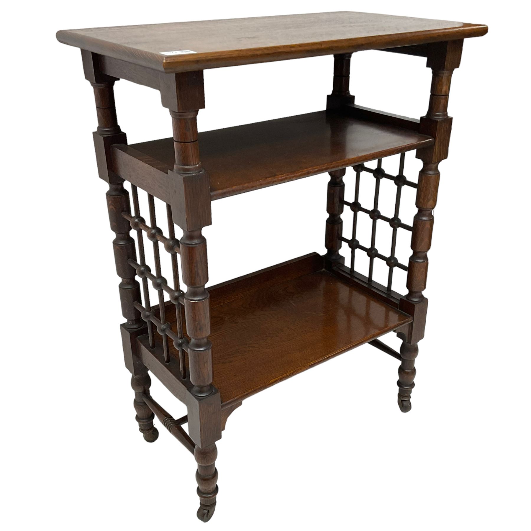 Late 19th century oak three-tier stand or bookcase, on turned supports with lattice sides, on turned feet with castors