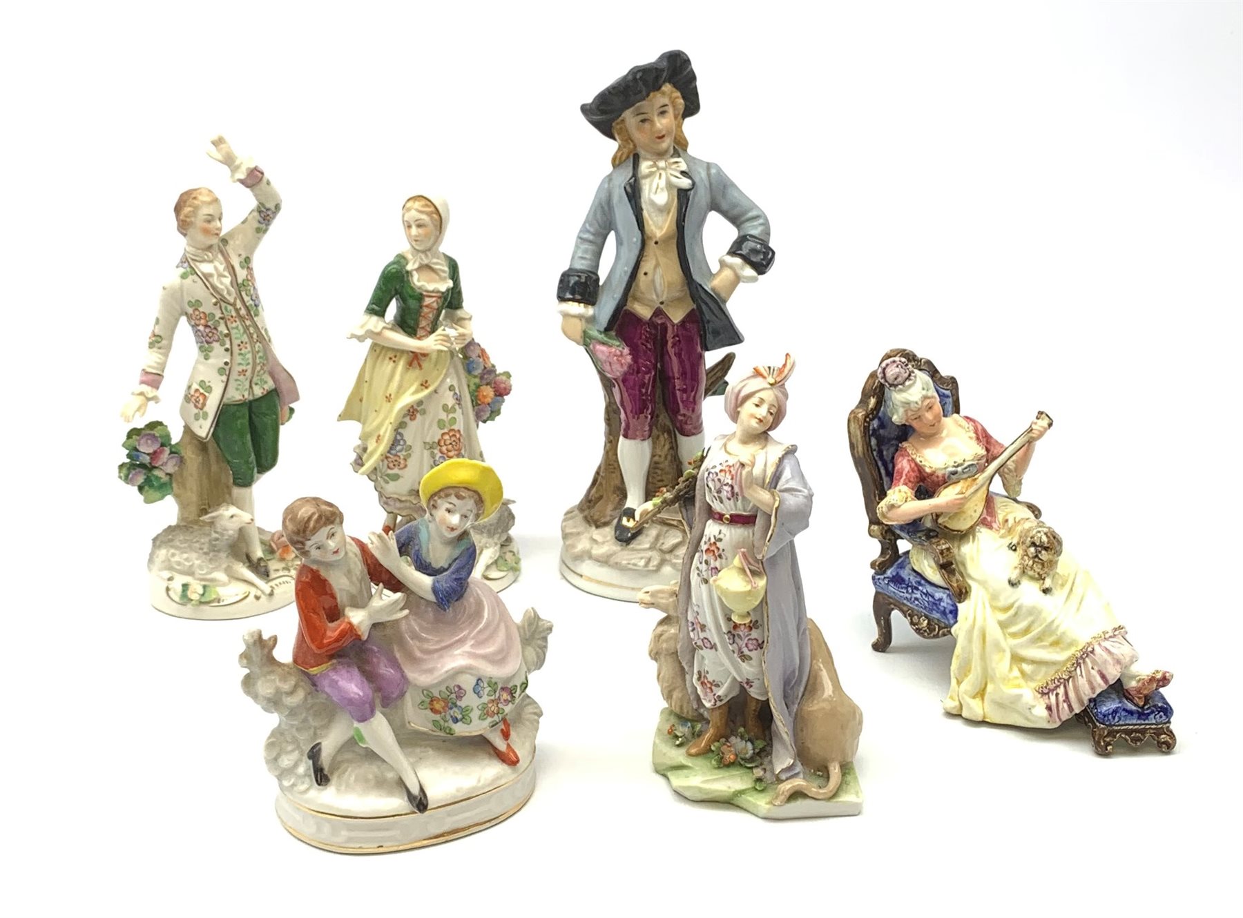 A pair of Sitzendorf figures, modelled as a male and female figure in eighteenth century dress with sheep beside feet, each upon gilt detailed circular base, each with printed mark beneath, tallest H18.5cm, together with a Volkstedt figure modelled as a Eastern female figure with camel seated at her feet, with printed mark beneath, a Sitzendorf figure of a young male figure, a figure modelled as a seated female playing the lute, with dog seated upon her lap, and a figure group marked foreign. (6). 