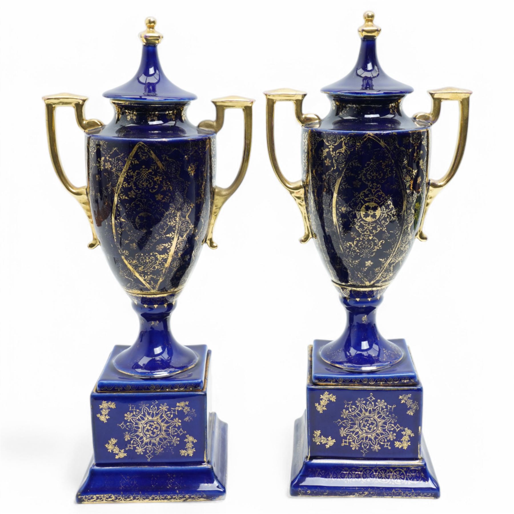 Pair of Vienna style blue porcelain two handled vases and covers painted with classical scenes on a dark blue and gilt ground and square socles, blue beehive mark H35cm