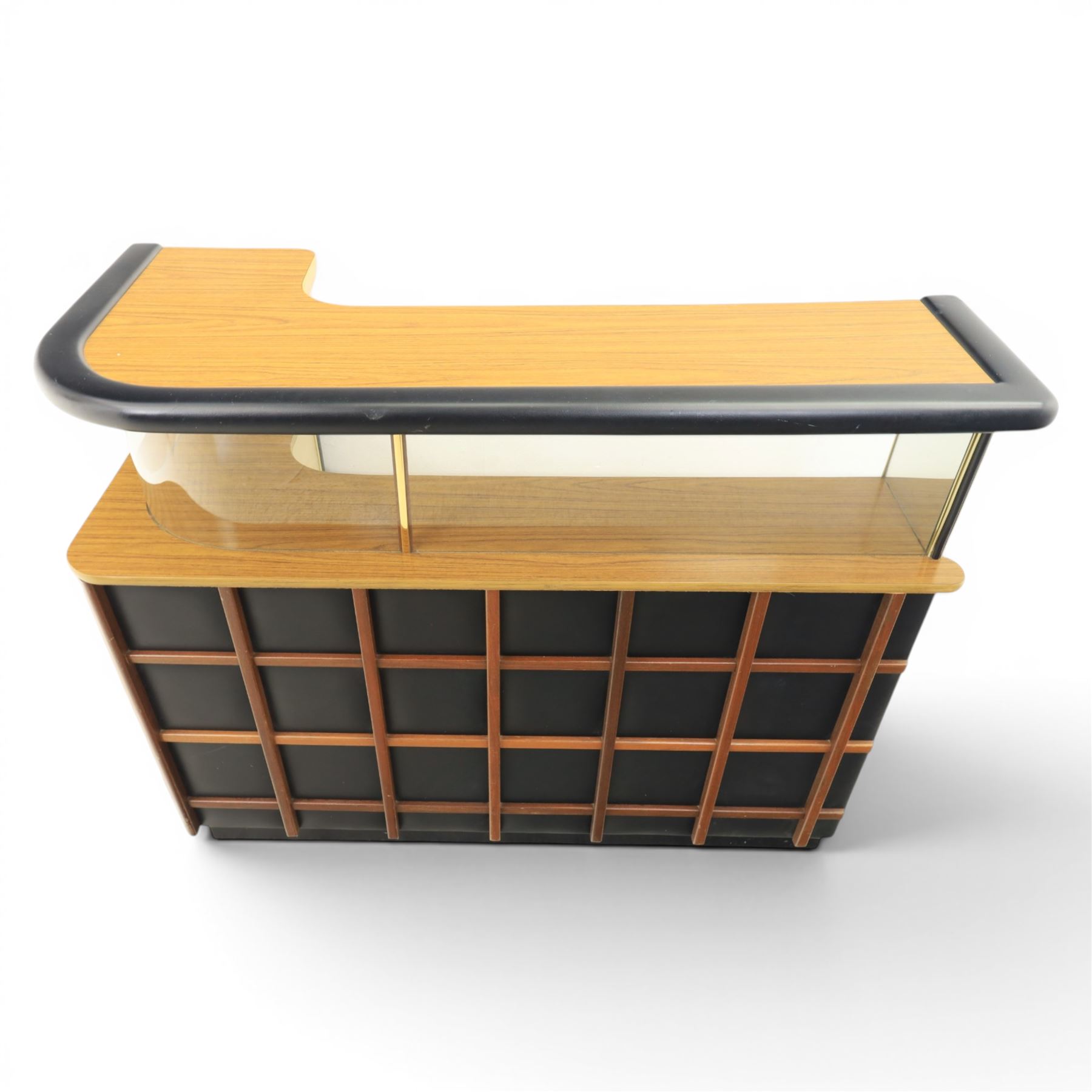Barget of London - Mid 20th century L-shaped teak and black vinyl cocktail bar, shaped top with gilt metal banding and black cushioned edge over glazed upper section and open serving shelf, the reverse fitted with shelves, the front with applied lattice mouldings over black vinyl, on plinth base