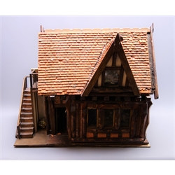  Wooden model of a Tudor style public house, with simulated beam/plaster and brick walls under a tiled roof with dormer window, the removable front revealing a fully furnished single room with figures, bar stools etc, external staircase with 'outside privy' under, leading to a furnished room in the roof space, wired for electricity, W57cm H47cm D34cm  