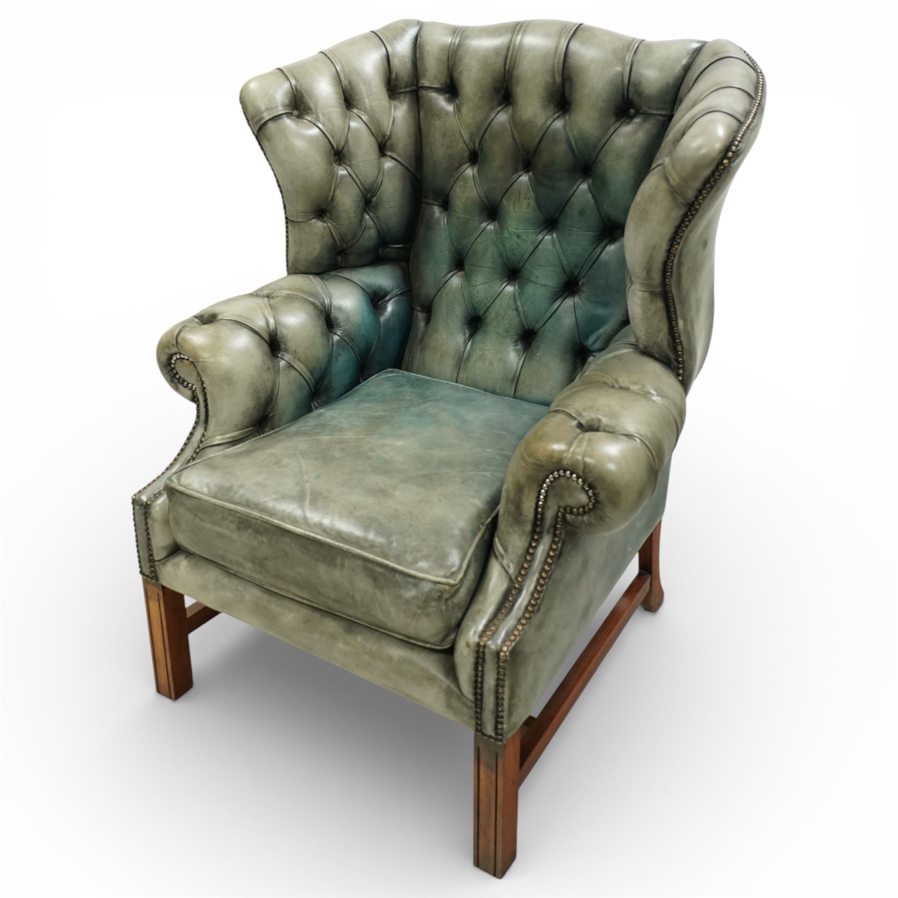 Georgian design mahogany framed wingback armchair, upholstered in rustic pale green buttoned leather with loose seat cushion, raised on square supports united by H-stretcher