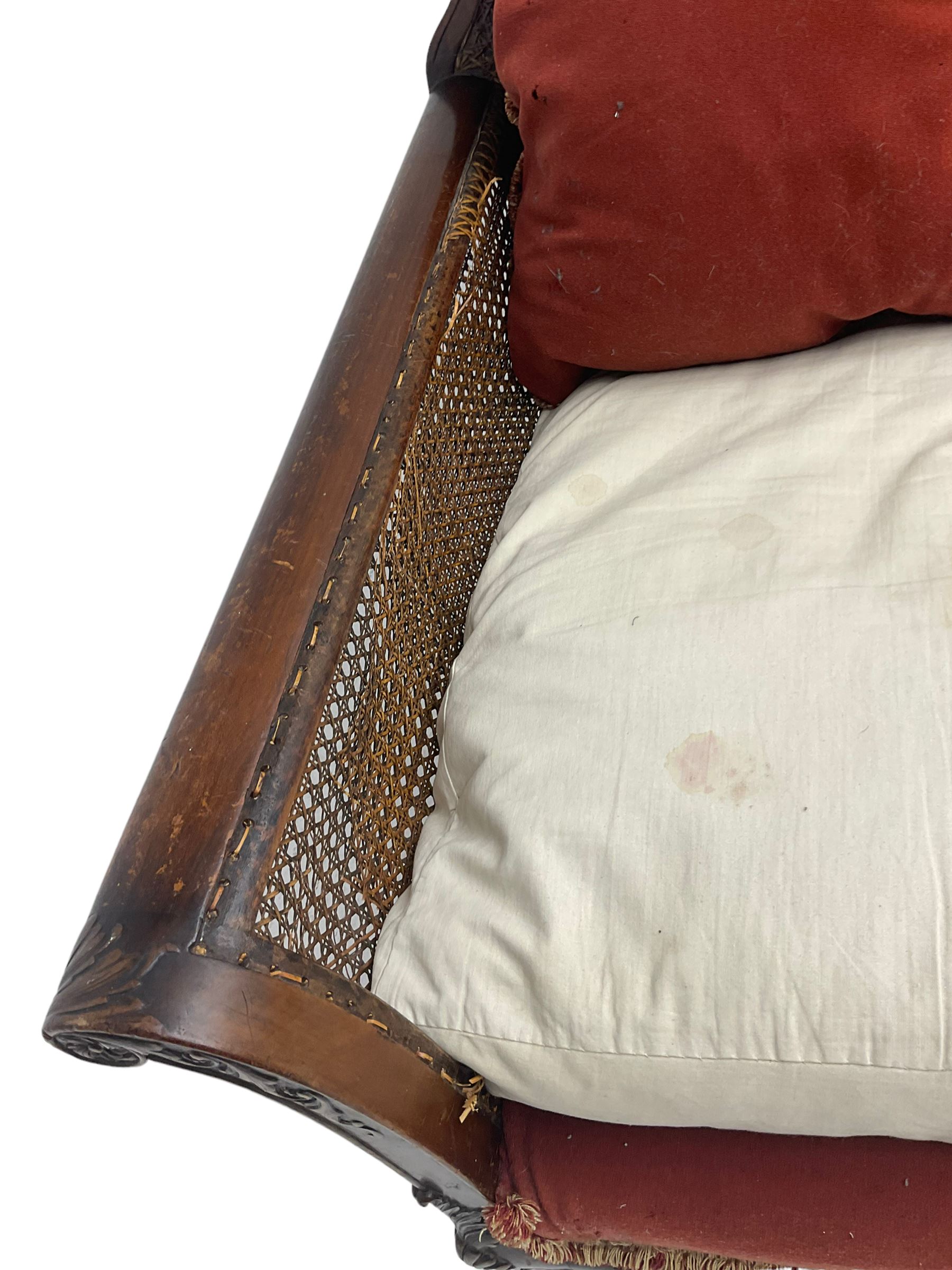 Early 20th century bergère three seat settee, shaped shell carved cresting rail, double caned back and sides, scrolled upright arms and shaped apron carved with shell and foliage, on hairy paw carved feet