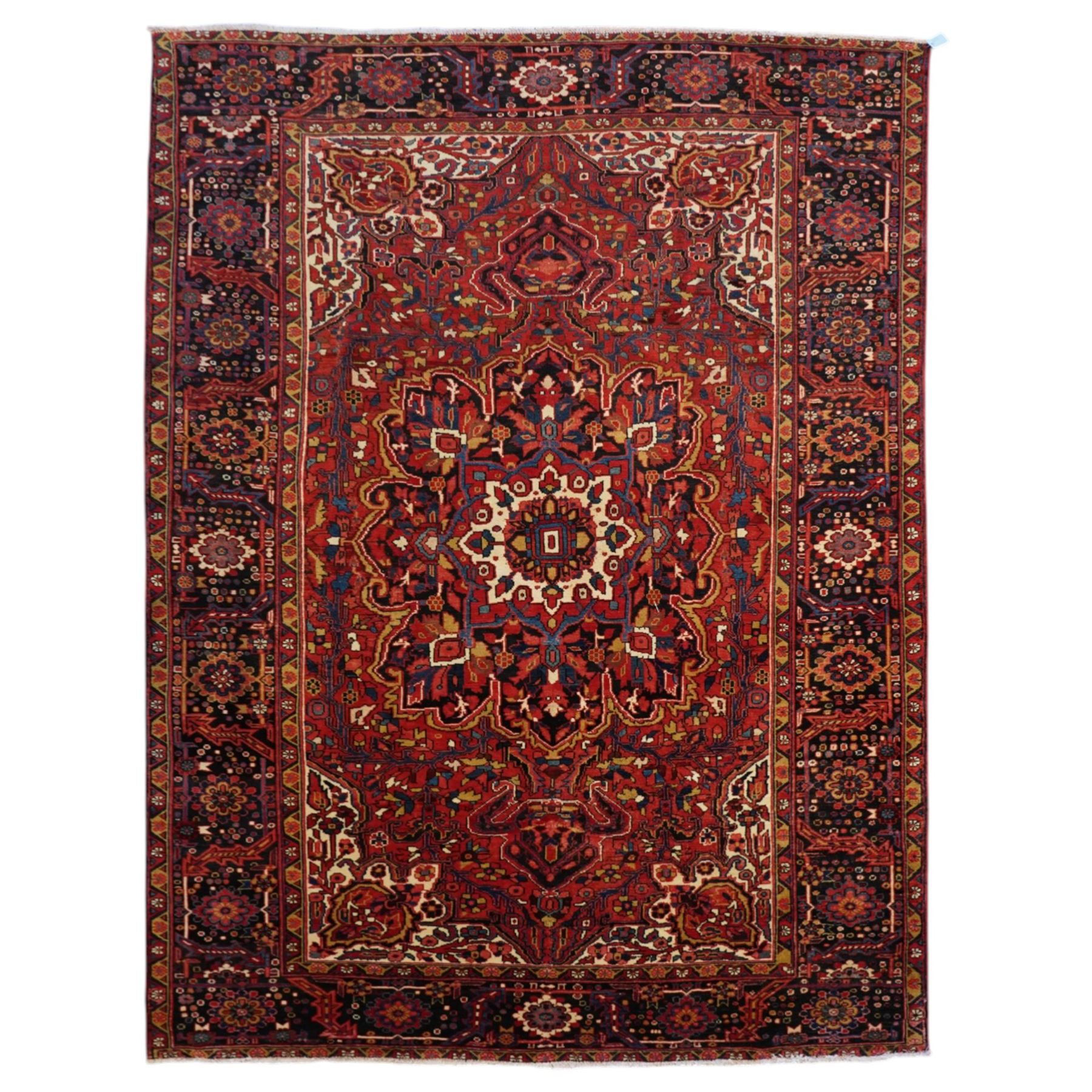 North West Persian Heriz/Ahar hand-knotted carpet, brick-red field with a large central angular stepped medallion with pendant motifs, surrounded by stylized palmettes, serrated leaves and geometric floral devices , ivory corner spandrels, enclosed by a dark indigo main border of stylized rosettes and angular vine motifs, between multiple guard stripes, with cotton fringe ends 