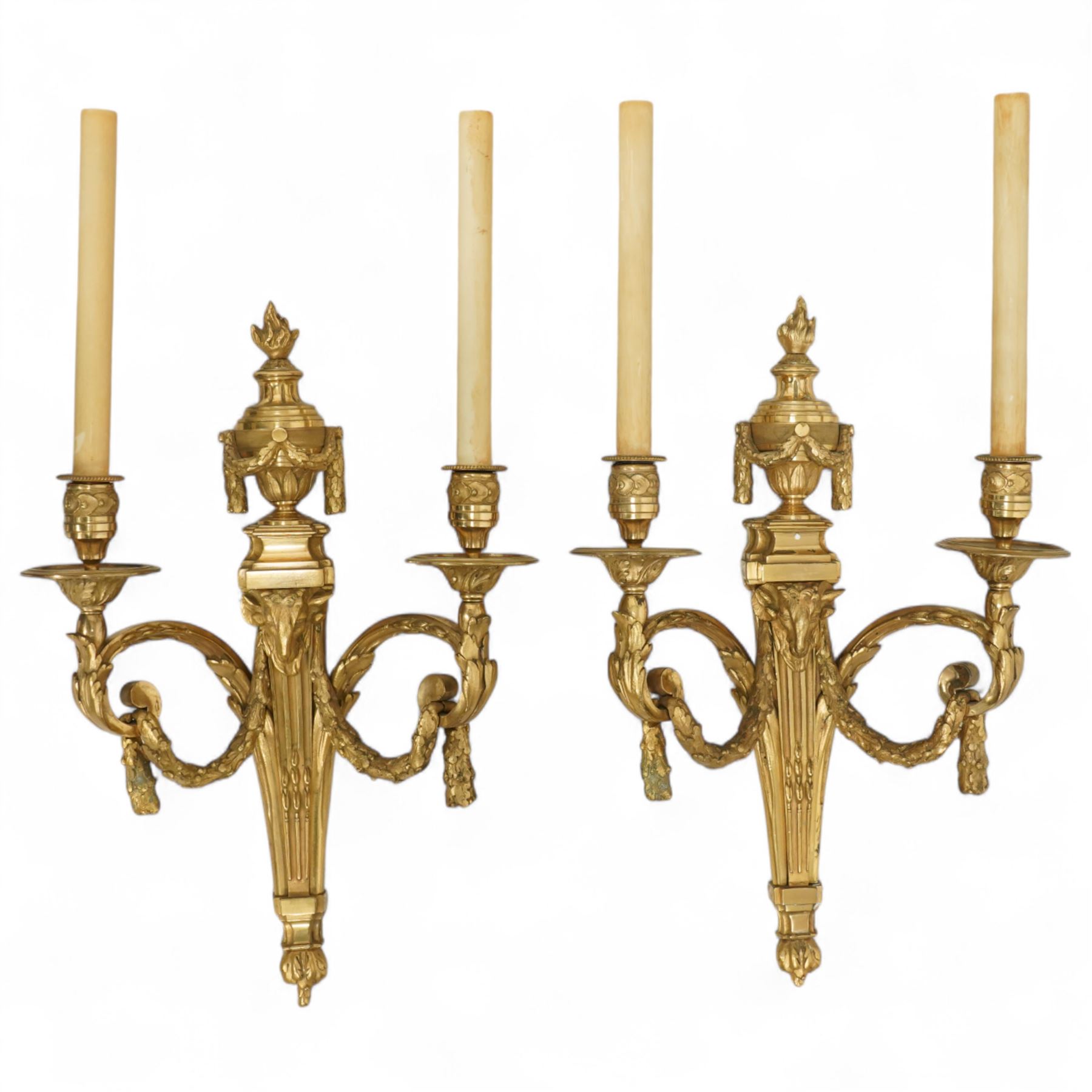 Pair of 19th-century Louis XVI-style ormolu rams-headed two-light wall appliques, the arms joined by a garland of laurel leaves, the half fluted stem surmounted by a vase with laurel garland, wired for electricity 