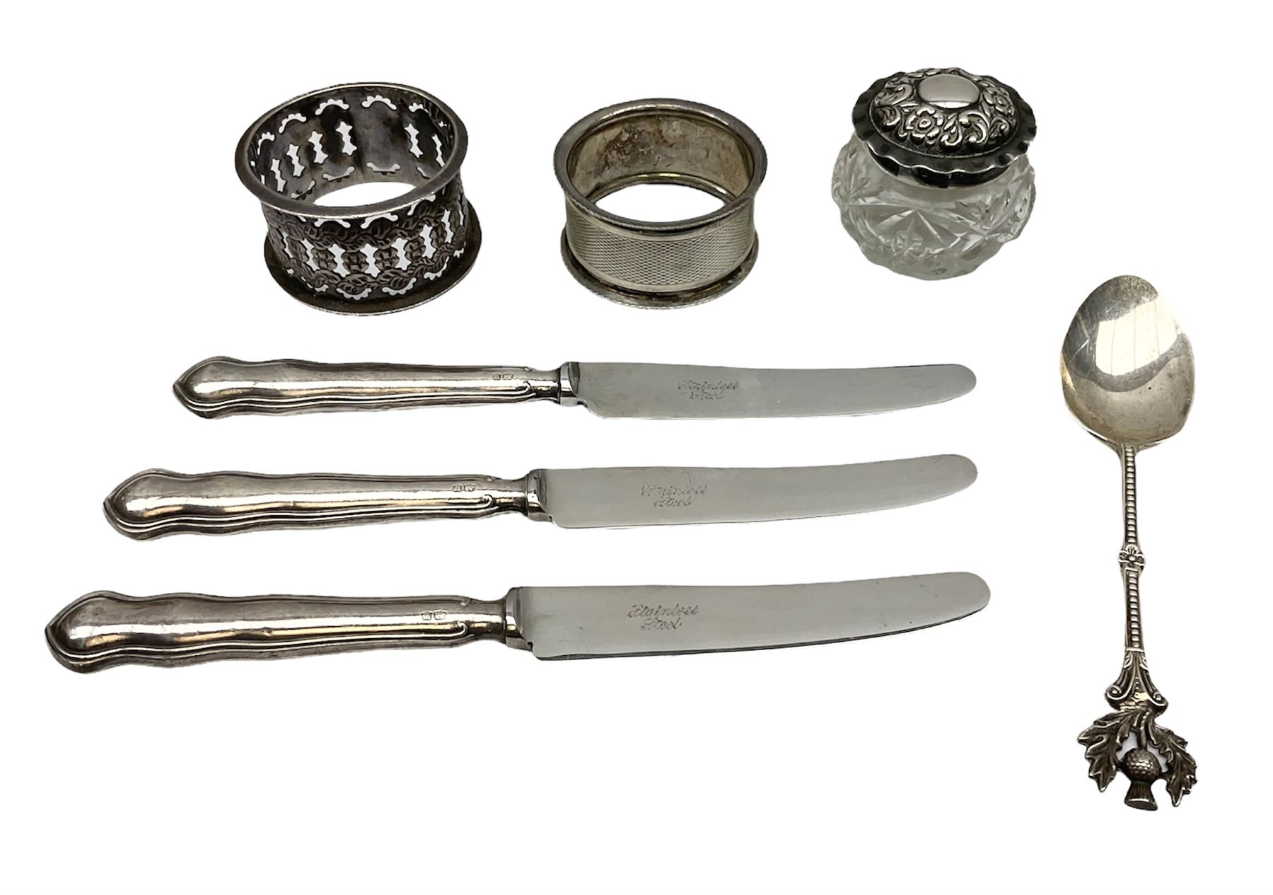 Two silver napkin rings, silver spoon with thistle top terminal, two silver handled butter knives, and small glass jar with silver cover, all hallmarked, approximate weighable silver 53.7 grams