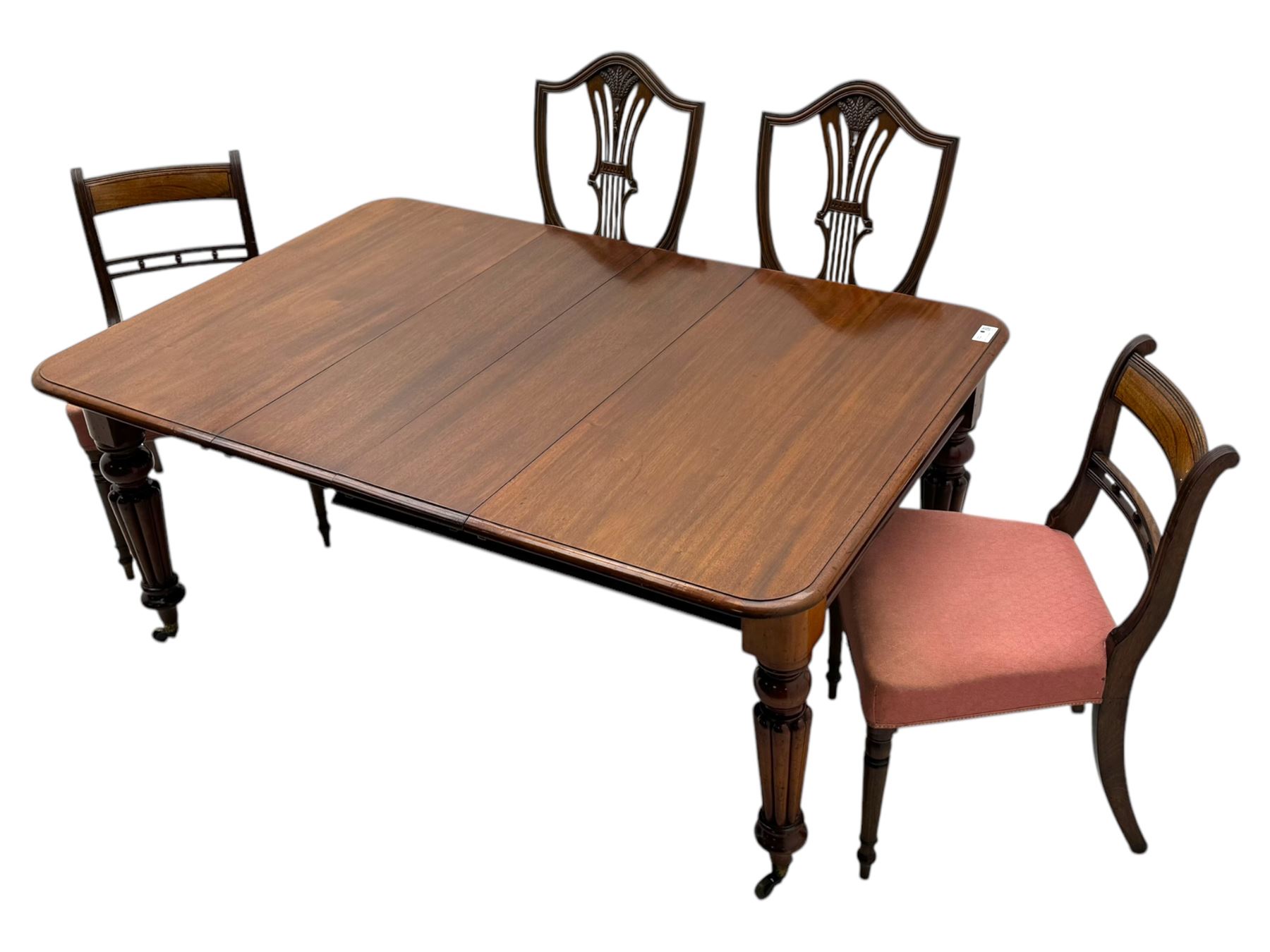 
Late Victorian mahogany extending dining table and four chairs, rectangular top with rounded corners and moulded edge, fitted with two additional leaves, raised on turned and reeded legs with brass castors, with a pair of Victorian mahogany hall chair, with curved top rail and plain splat, padded seat in textured salmon pink fabric, raised on turned and tapering front legs and another pair of early 20th century mahogany dining chair, with shield back and carved pierced splat, serpentine seat rail with striped upholstered cushion, raised on moulded square front legs