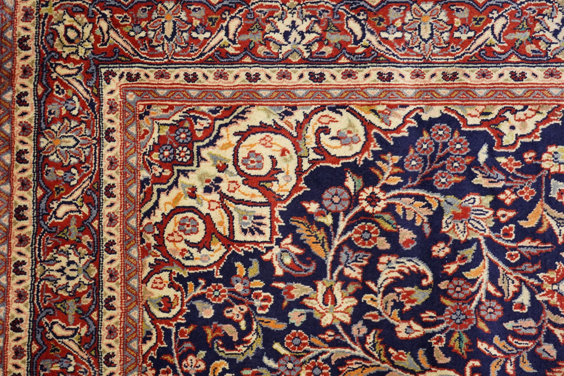 Central Persian Kashan hand-knotted rug, indigo field with central lobed medallion with pendants issuing scrolling arabesque of palmettes, flowering vines, and foliate tendrils, with conforming spandrels, with vine border and framed by guard stripes in tones indigo, ivory and madder red, with cotton fringe ends 