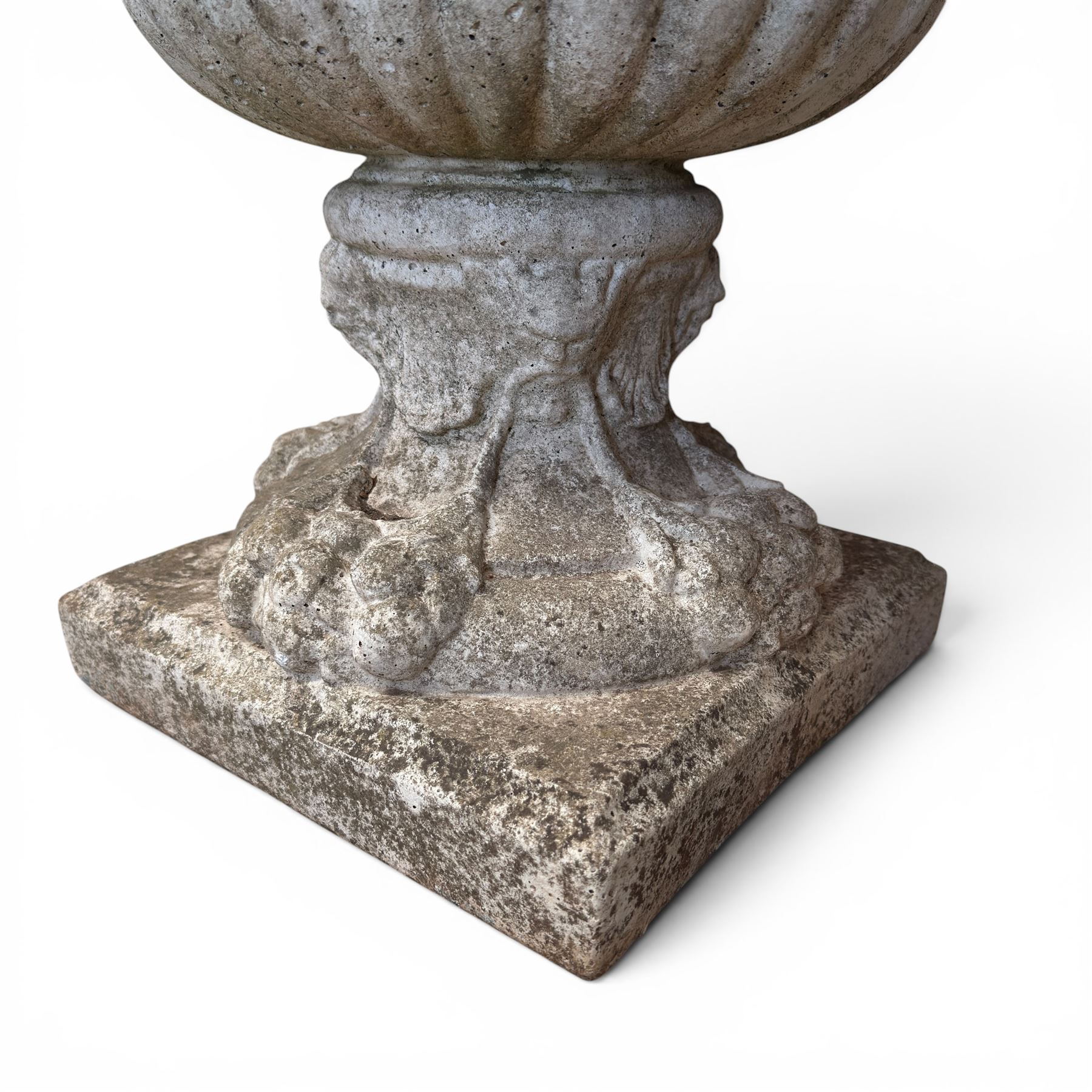 Pair of Neoclassical design cast stone garden urns, each of campana form with fluted body and gadrooned underbelly, decorated with faun/satyr opposing masks and ropetwist handles, with floral and mask design to the socles, raised on square bases, finished in weathered white patina