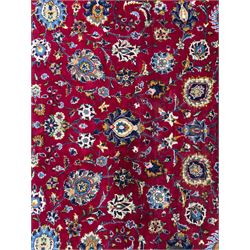 Northeastern Persian Meshed hand-knotted carpet, madder red field with an all-over design of scrolling vines, palmettes, and rosettes, within a dark blue border of palmettes and arabesques 