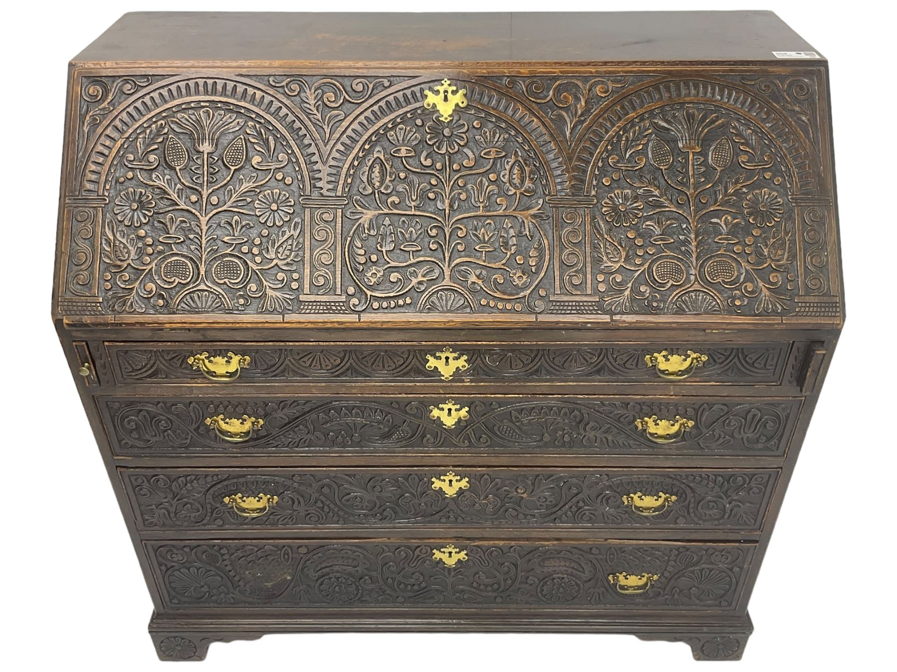 18th century heavily carved oak bureau, the fall front relief carved with three arches enclosing plants and flower head decoration, the interior fitted with pigeonholes, drawers and cupboard, four graduating cock-beaded drawers below, carved with lunettes and trailing foliage decoration, on bracket feet