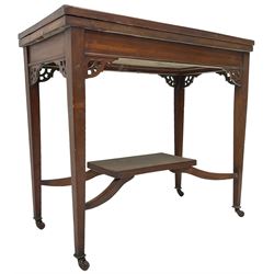 Edwardian inlaid mahogany games table, the rectangular fold-over swivel top decorated with central shell motif inlay and ebony stringing, raised on tapering supports united by shaped X-stretcher and undertier