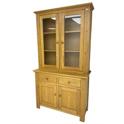 Contemporary light oak bookcase display cabinet, fitted with  two glazed doors enclosing two shelves, above two drawers and cupboards