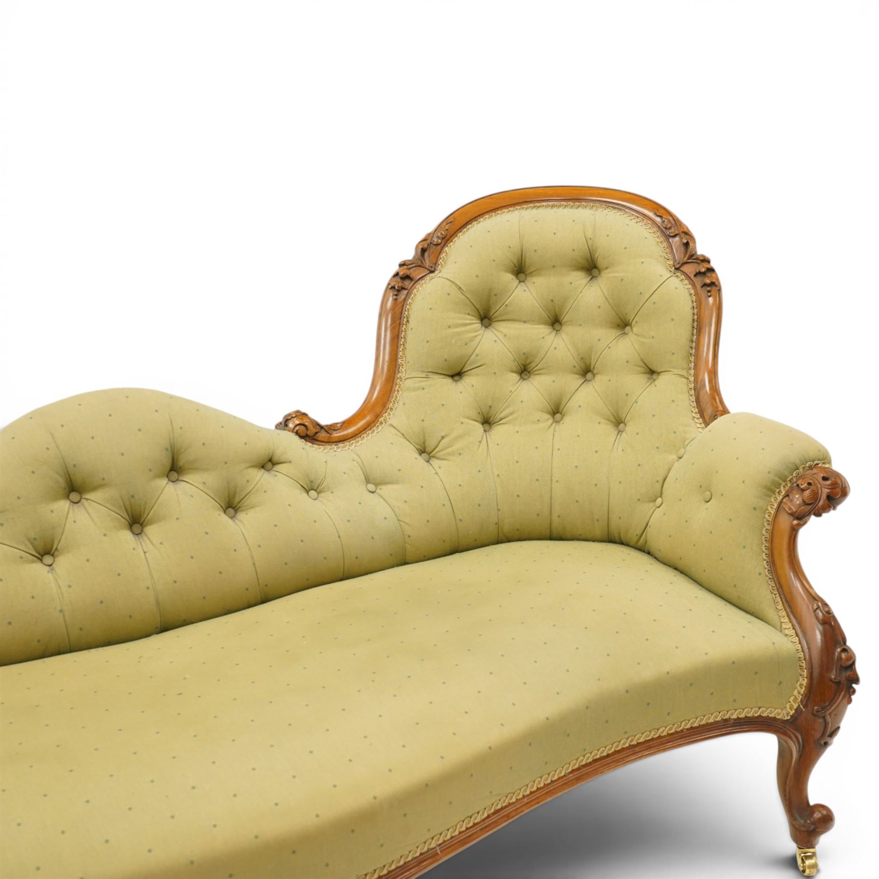 Victorian mahogany framed double ended chaise longue, serpentine button upholstered back with raised scrolled ends, padded arms and stuff-over seat upholstered in green fabric, carved showframe with foliate terminals and scroll supports, on short cabriole legs with brass castors
