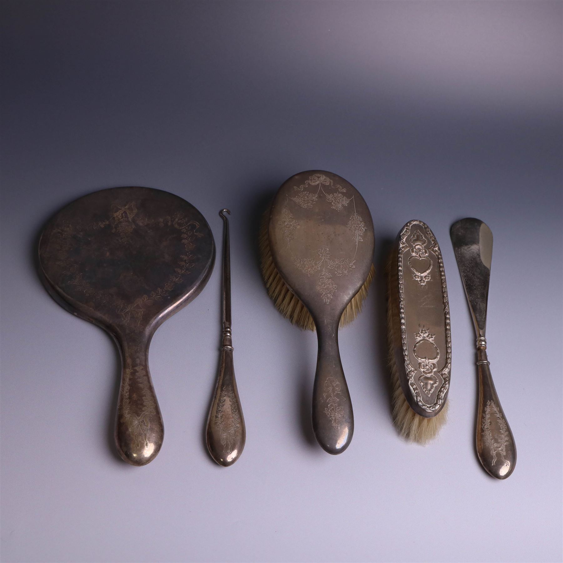 Early 20th Century silver mounted dressing table set, comprising hand mirror, shoe horn and a button hook, each with engraved floral decoration, together with a silver mounted hairbrush and clothes brush, all hallmarked