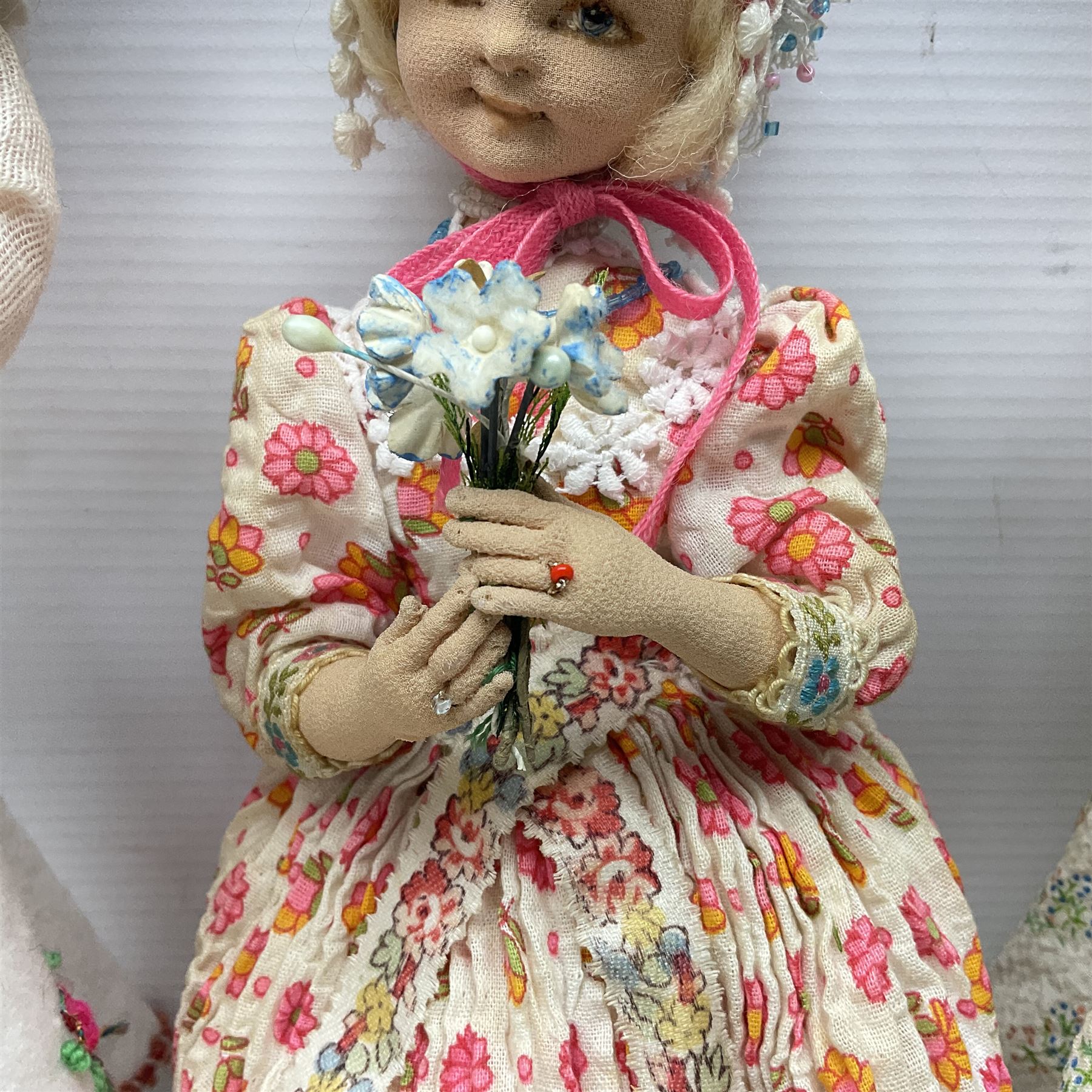 Anna Meszaros Hungary - three hand made needlewrok figurines - each wearing a lon floral dress and bonnet and holding a bouquet of flowers, tallest H32cm (3)  Auctioneer's Note: Anna Meszaros came to England from her native Hungary in 1959 to marry an English businessman she met while demonstrating her art at the 1958 Brussels Exhibition. Shortly before she left for England she was awarded the title of Folk Artist Master by the Hungarian Government. Anna was a gifted painter of mainly portraits and sculptress before starting to make her figurines which are completely hand made and unique, each with a character and expression of its own. The hands, feet and face are sculptured by layering the material and pulling the features into place with needle and thread. She died in Hull in 1998.