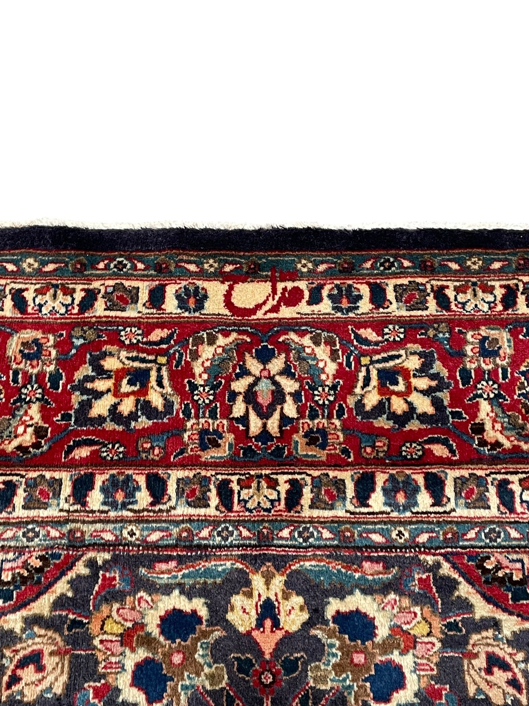 Persian Kashan indigo ground carpet, large central rosette medallion decorated with alternating palmettes, the surrounding field and spandrels with overall floral design depicting trailing branches and stylised plant motifs, crimson ground border with trailing floral pattern, enclosed within guard stripes 