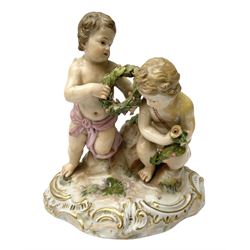 Meissen figure group modelled as two putto, one holding olive wreath and each kneeling upon a naturalistically modelled base also detailed with gilt C scrolls, with underglaze blue crossed swords mark beneath and impressed 2904, H12.5cm