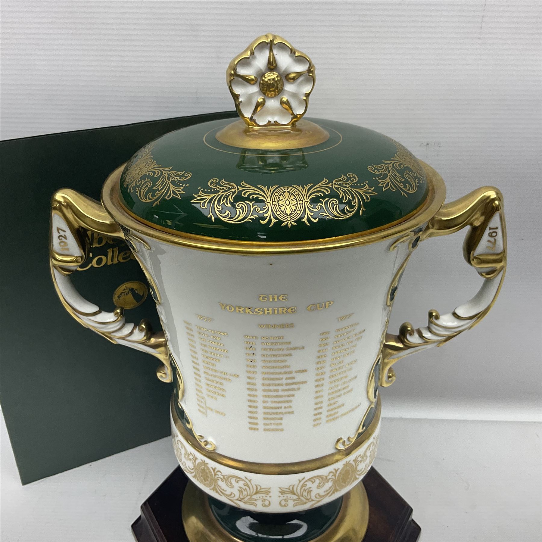 Aynsley twin handled racing cup and cover, to commemorate 'The Golden Jubilee of the Revival of The Yorkshire Cup', the handles inscribed '1927' and '1977', the green body painted by E. Woodhouse with Joe Childs up on Trimdon, the reverse with the winners, the domed cover with a Yorkshire rose finial, limited edition no. 4 of 50, on hexagonal wooden base with certificate, H34cm