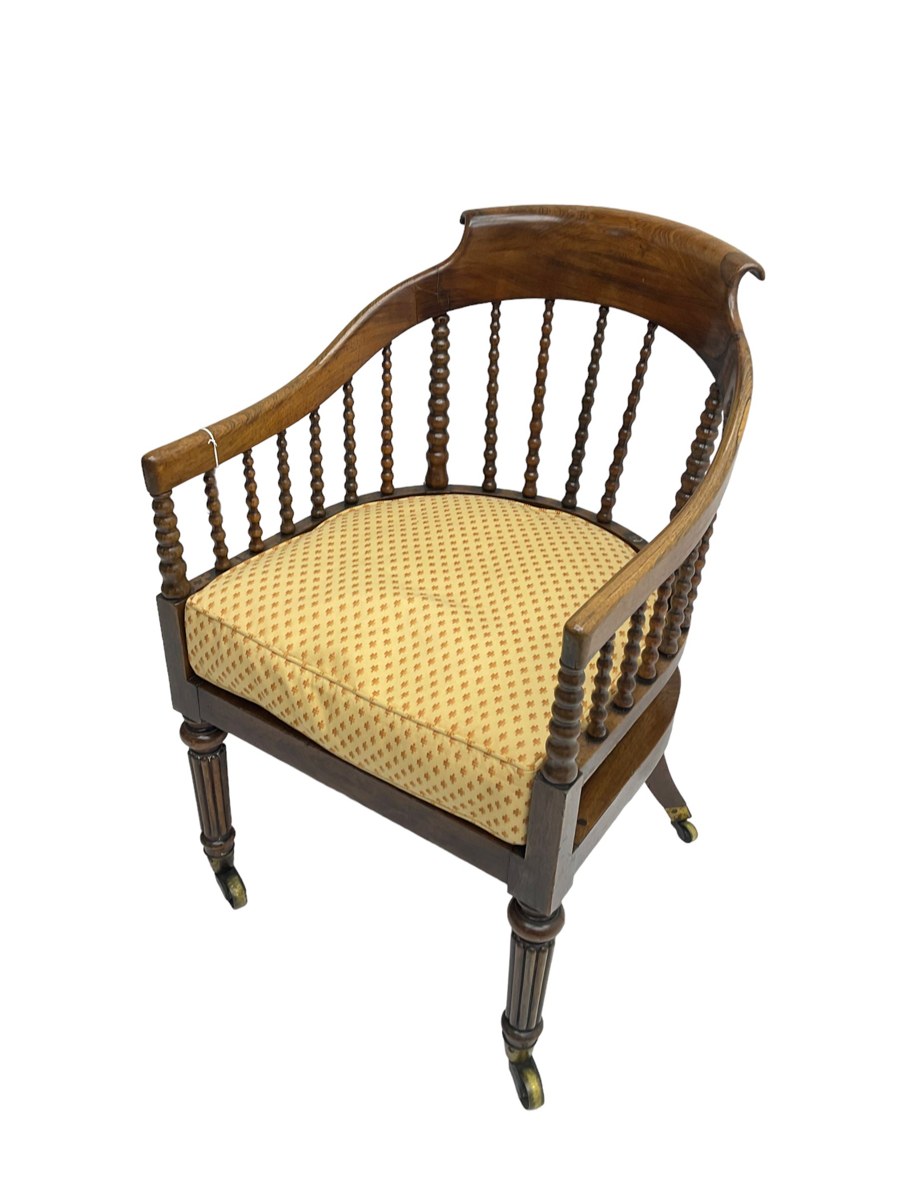 William IV rosewood tub armchair, the arched bow cresting rail over graduated bobbin turned spindles, cane seat with loose cushion, terminating in brass cups and castors.