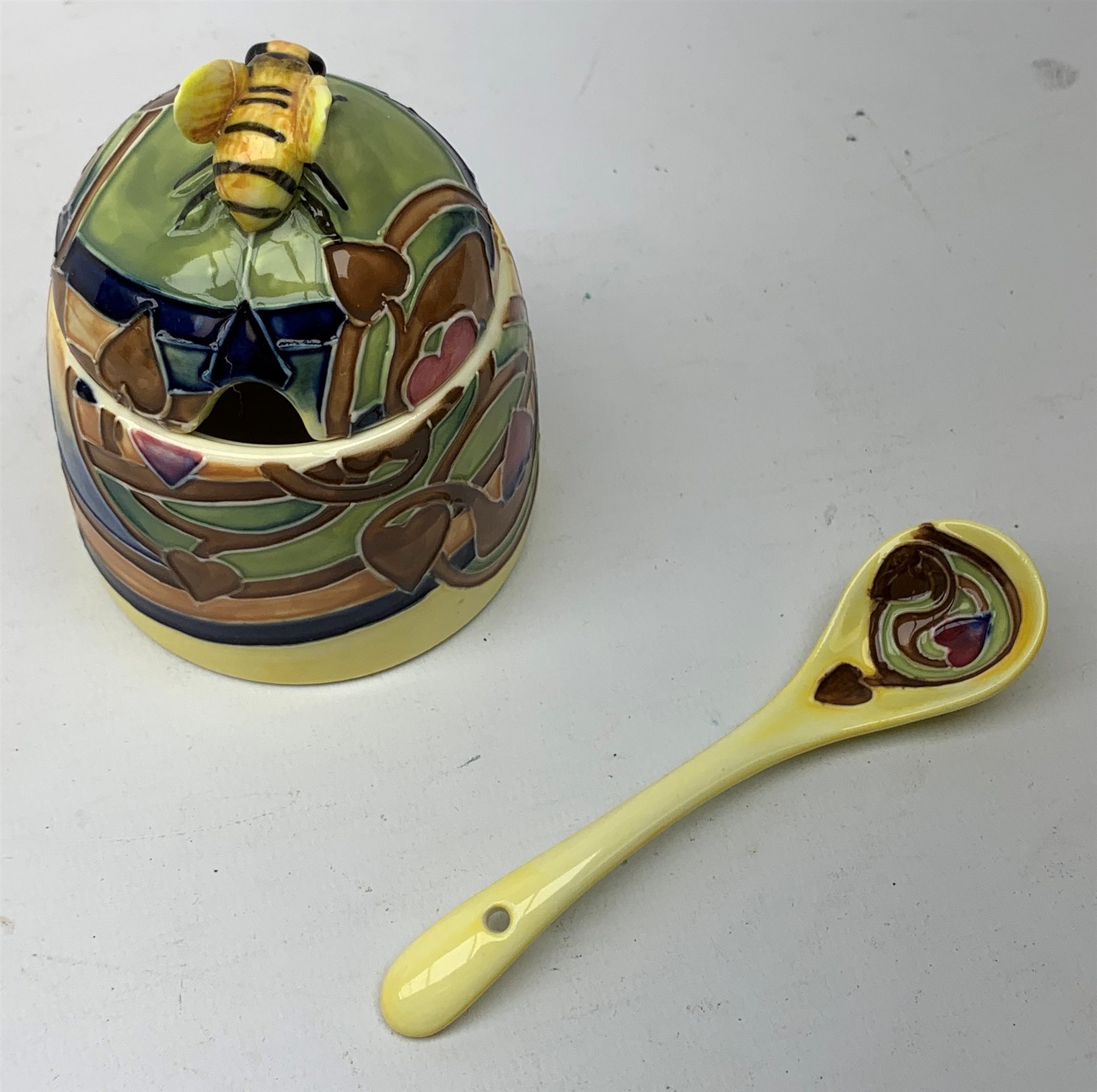 An Old Tupton Ware honey pot, of oval form with tube lined tendril decoration, the domed cover surmounted by a honey bee, with accompanying spoon, together with a pair of Old Tupton Ware vases, with tube lined sunflower decoration, H22cm, each with printed mark to base.
