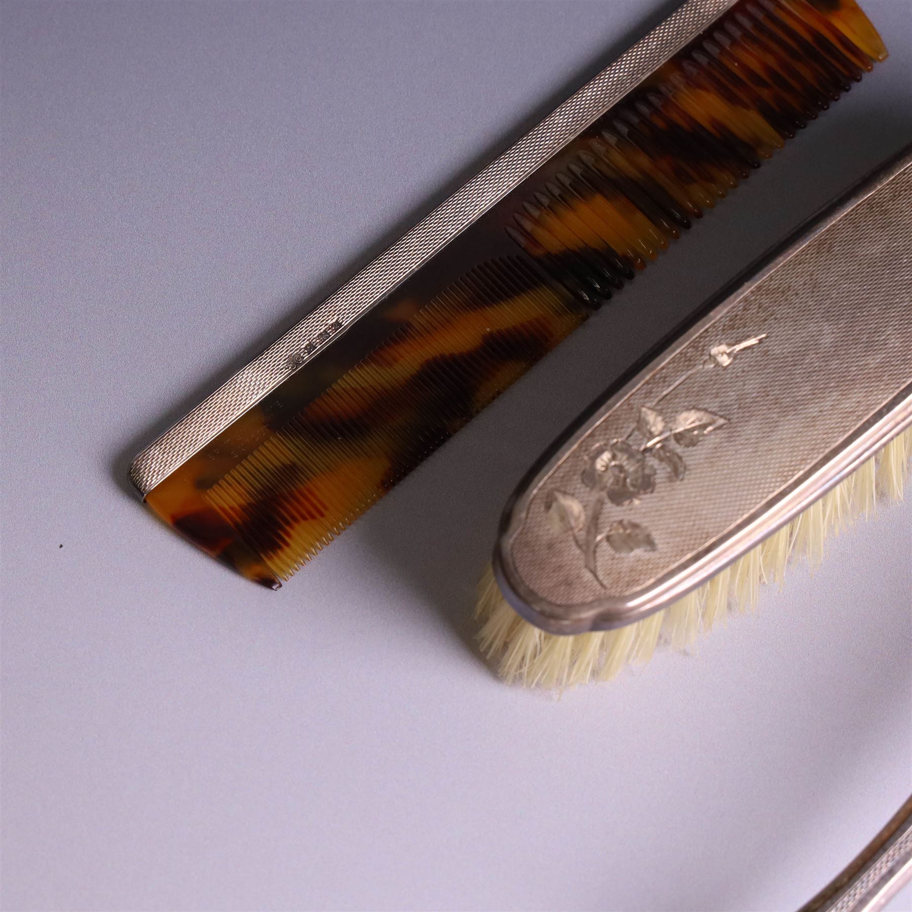 20th Century silver mounted dressing table set, comprising hand mirror, clothes brush, hairbrush and comb holder, each with engine turned and engraved floral decoration, three pieces hallmarked Adie Brothers Ltd Birmingham 1964, the comb holder hallmarked Elkington & Co Ltd Birmingham 1965, contained within a fitted tooled leather case