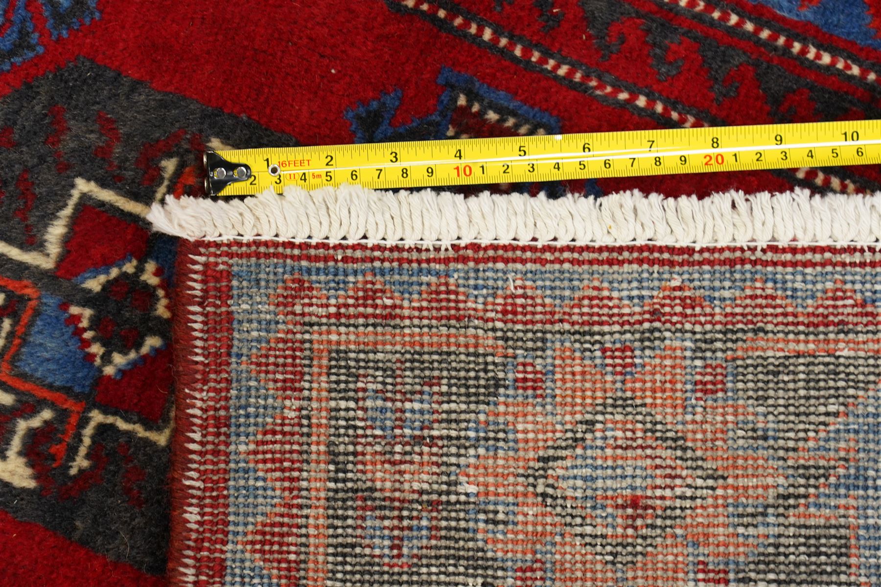 North East Persian Balochi hand-knotted runner, crimson field decorated with three vertical columns of repeating octagonal guls, each enclosing angular geometric motifs in deep indigo, ivory, and soft brown tones, guls linked by stepped diamond and cruciform devices, main border of stylized geometric floral motifs and angular vines, flanked by multiple guard borders, with cotton fringe ends 