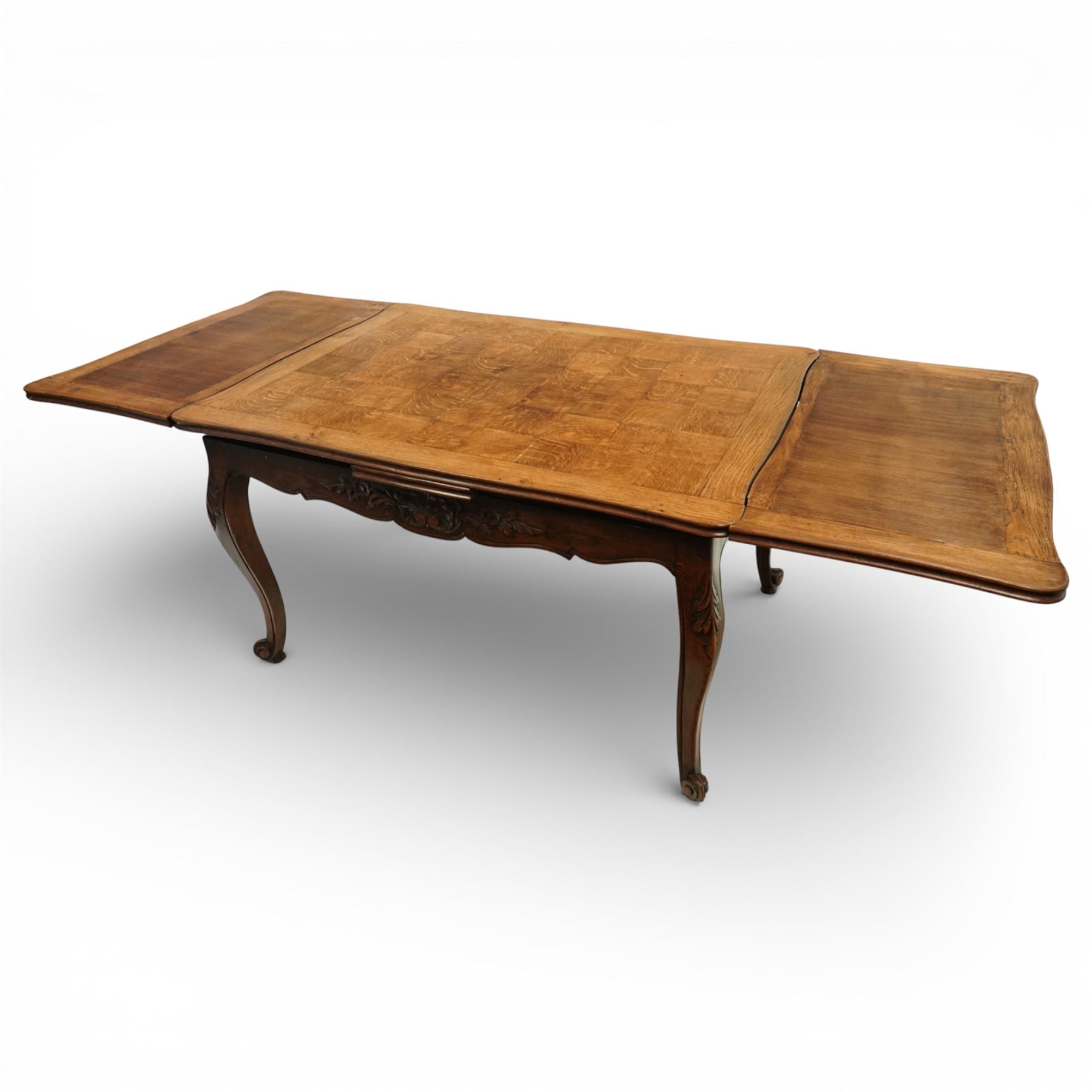 20th century French oak drawer-leaf extending dining table and six chairs, the rectangular parquetry top with moulded edge and rounded corners, pull-out draw leaves extending the table to 240cm, carved frieze with foliate detail, raised on cabriole supports with scroll terminals, the six matching chairs with shaped backs carved with floral motifs, paper cord seats woven with a green pattern, cabriole front supports and turned stretchers