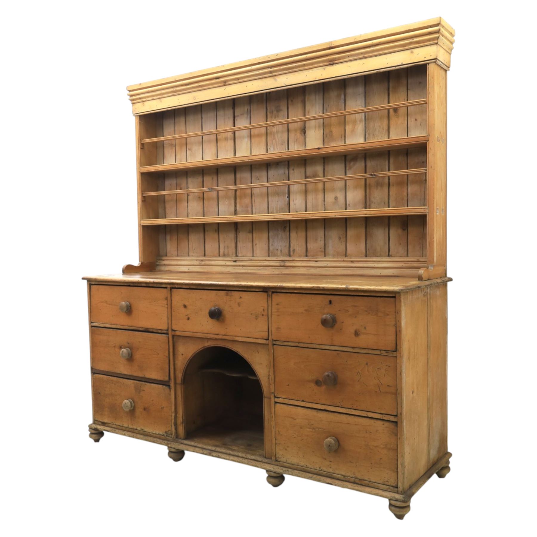 Early 19th century waxed pine farmhouse dresser and rack, the rack featuring two plate shelves and bars above seven drawer base with centre 'dog kennel' recess, raised on turned feet