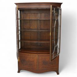 Edwardian mahogany and satinwood bow-fronted display cabinet, moulded dentil cornice over two astragal glazed doors, fitted with three shelves, double cupboard below, the doors inlaid with figured oval panels and satinwood bands, shaped apron on splayed bracket feet 