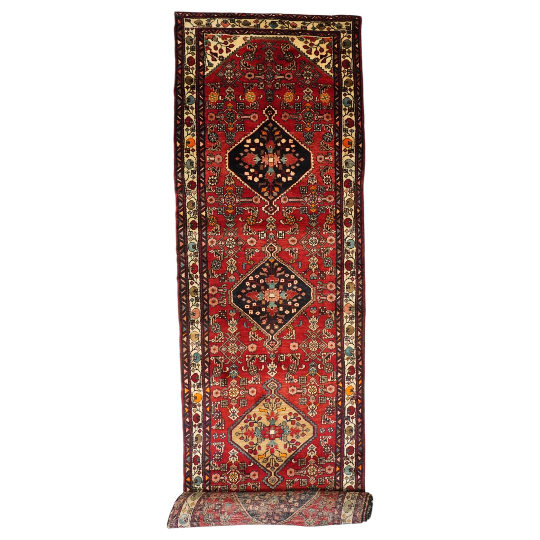 Large Persian Qashqai runner rug, the red ground decorated with navy and ivory lozenge medallions interspersed with stylised floral and geometric motifs, enclosed by an ivory flowerhead border and patterned guard stripes