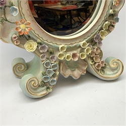  A late 19th century Sitzendorf porcelain mirror, the mirror plate of circular form set within a shaped surround encrusted with flowers and foliage, surmounted by three figures of cherubs and raised upon four scroll feet, with blue cross hatch mark beneath, H57cm.   