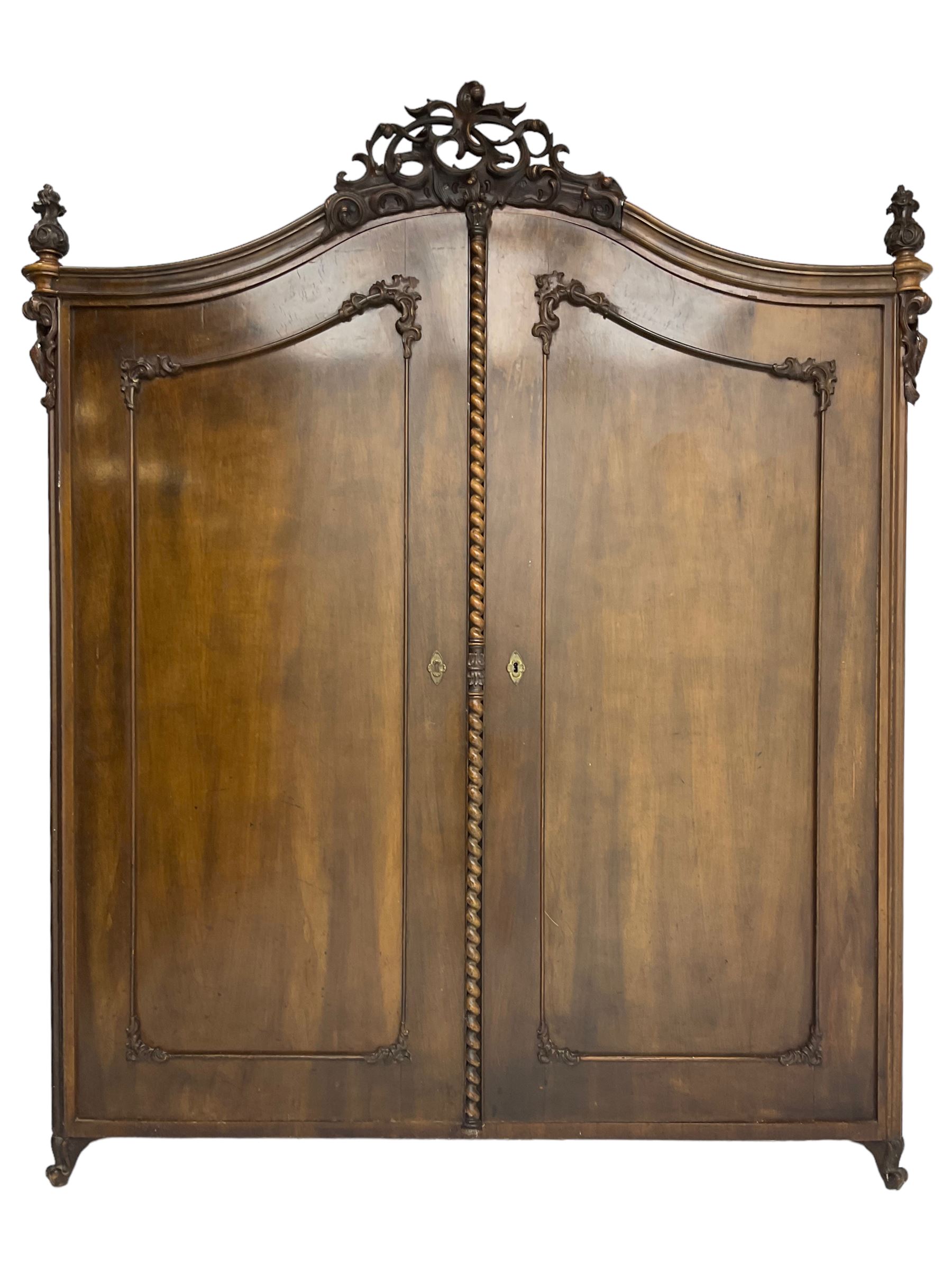 Early 20th century Italian walnut armoire wardrobe, the pierced and scrolling pediment carved with acanthus leaf detail, flanked by two scrolling cartouche with matching corbels below, the two panelled doors with applied carved rinceaux slips, with a central spiral turned upright, enclosing single shelf and hooks, raised on scroll feet