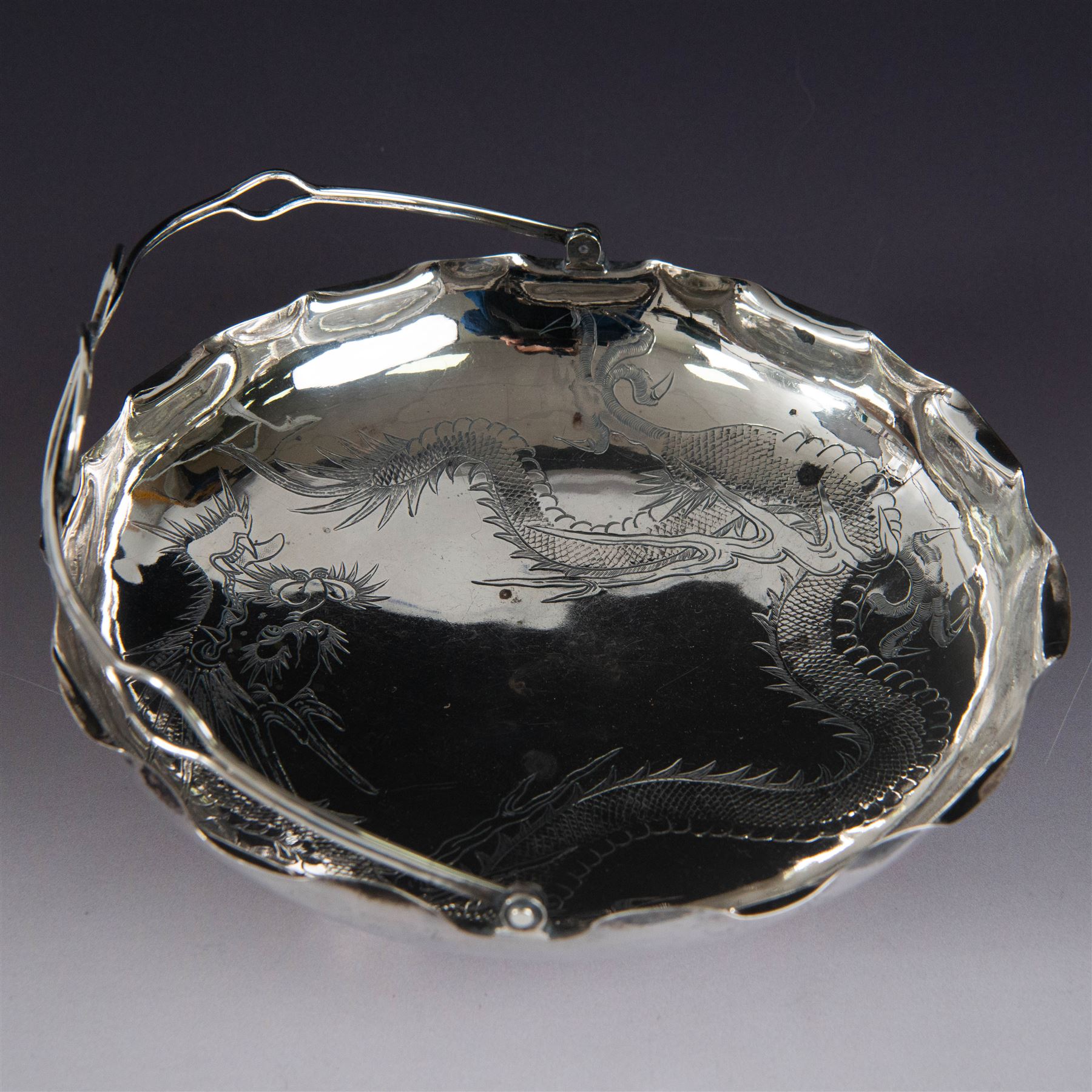Chinese export silver swing handled basket, of circular for with crimped rim and knotted wirework handle, engraved with a dragon to centre, upon three bun feet, with maker's mark T.H, character marks and 95 to underside, including handle H17cm