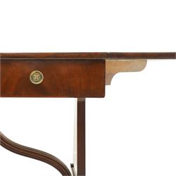 Early 20th century Regency Revival figured mahogany sofa table, rectangular drop-leaf top with rounded corners, fitted with two drawers to each side with brass flowerhead pull handles, raised on twin end supports with splayed reeded legs and brass cups and castors, united by a scrolling and reeded closed stretcher