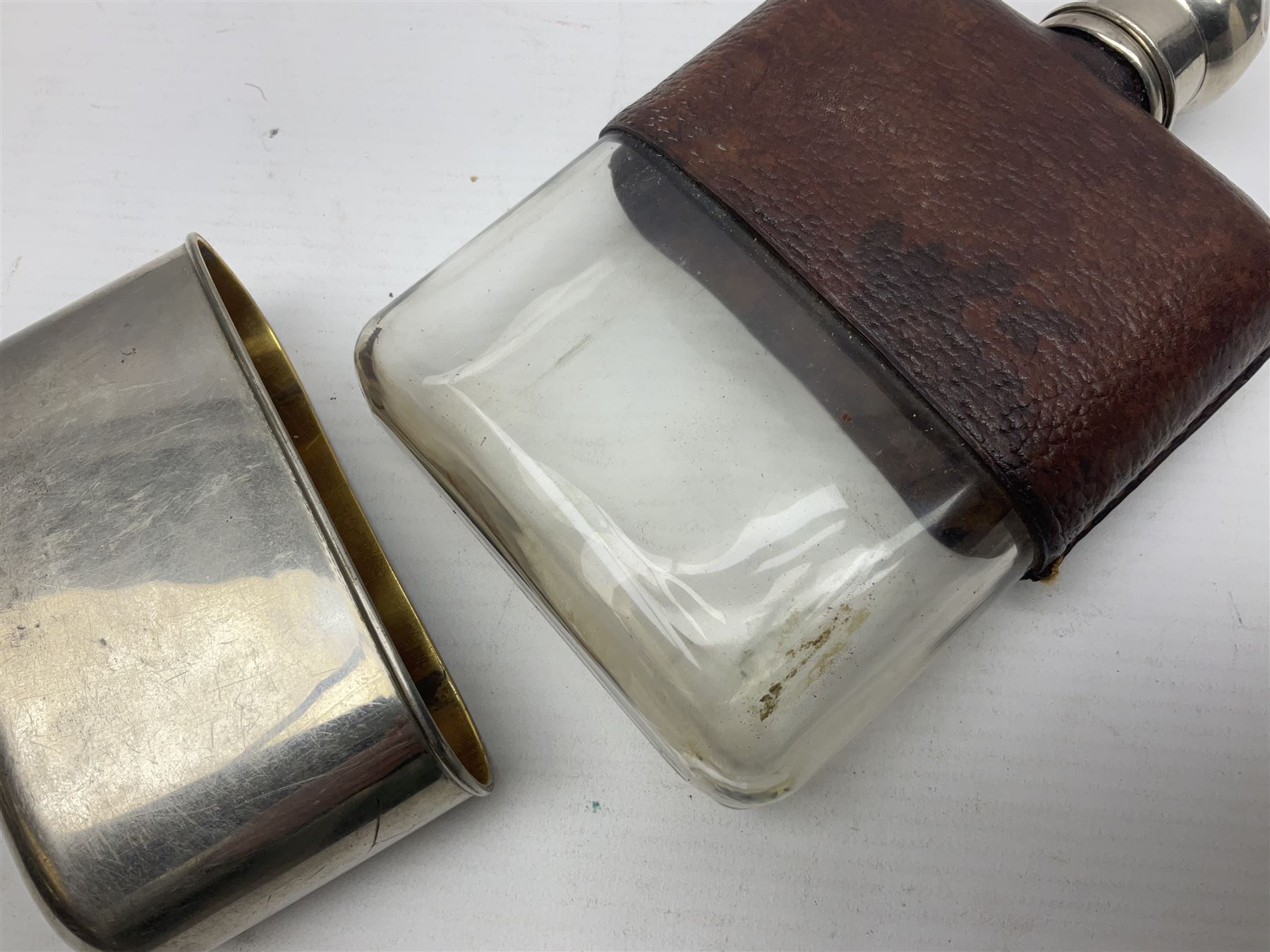 Silver plated glass and pressed leather hip flask, with swivel cap and removable cup, together with a similar oval example, engraved with wreath and initial B, tallest H16.5cm