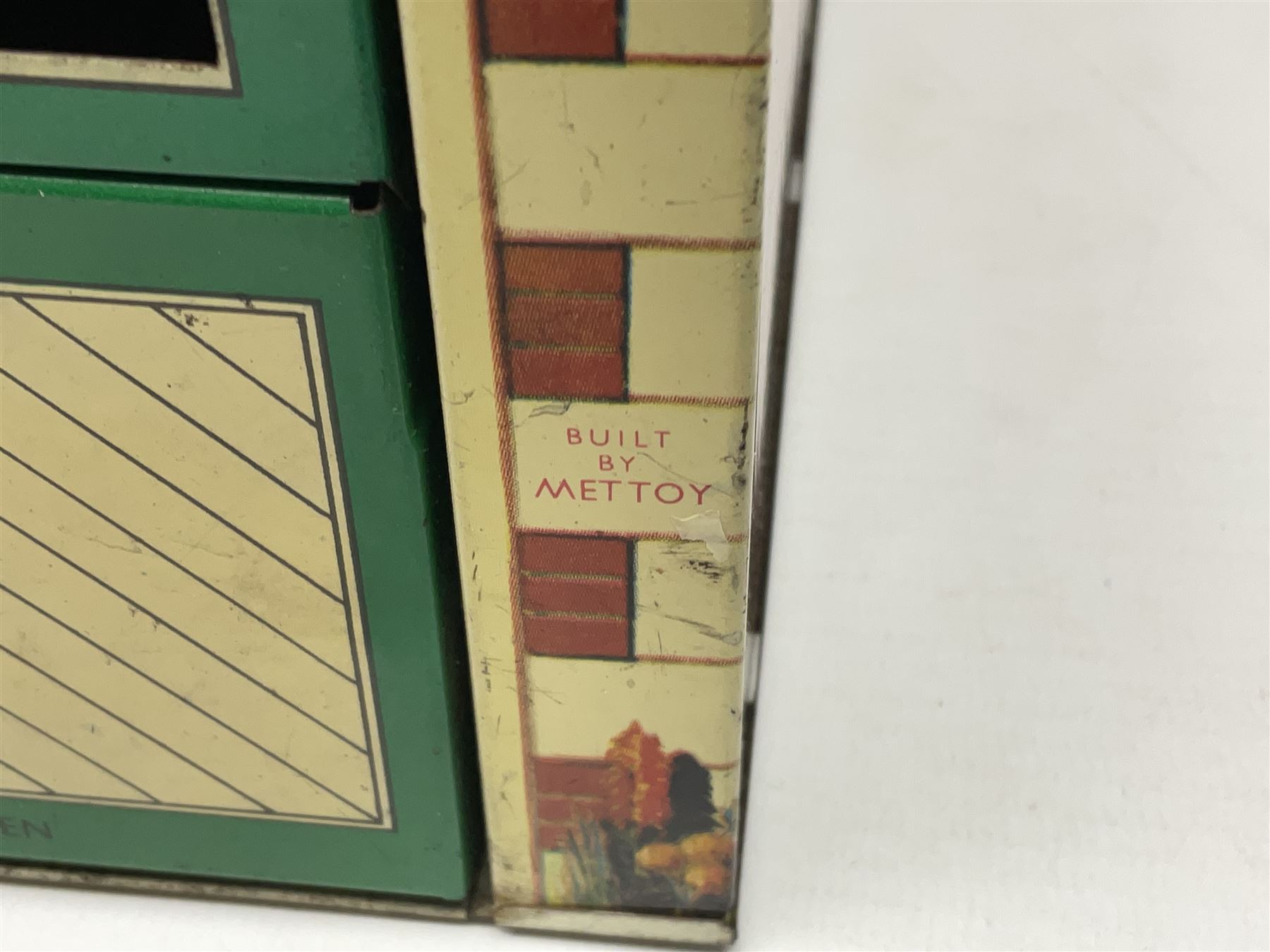 Mid-20th century Mettoy tin-plate double-fronted two-storey doll's house, the front elevation with five unglazed windows flanked by green shutters, central opening door, open back giving access to five rooms together with an attached garage, 60cm wide