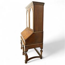 Queen Anne burr walnut chest on stand, moulded projecting cornice over arched mirror glazed doors, above a sloping fall front enclosing fitted interior with pigeonholes and correspondence drawers, fitted with foliate brass escutcheons, shaped apron over tapered baluster turned supports united by curved stretchers, early 18th century with later restorations 