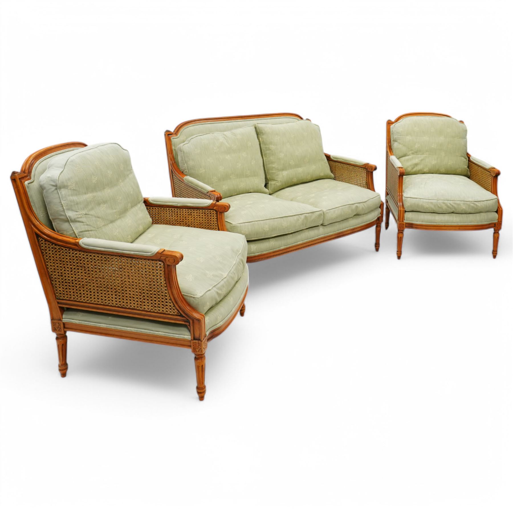 French Empire design varnished wood three piece lounge suite comprising of two cane armchairs and matching sofa, carved top rails with foliate terminals, cane side panels and padded scroll arms, upholstered in a green brocade with matching piping, on fluted legs