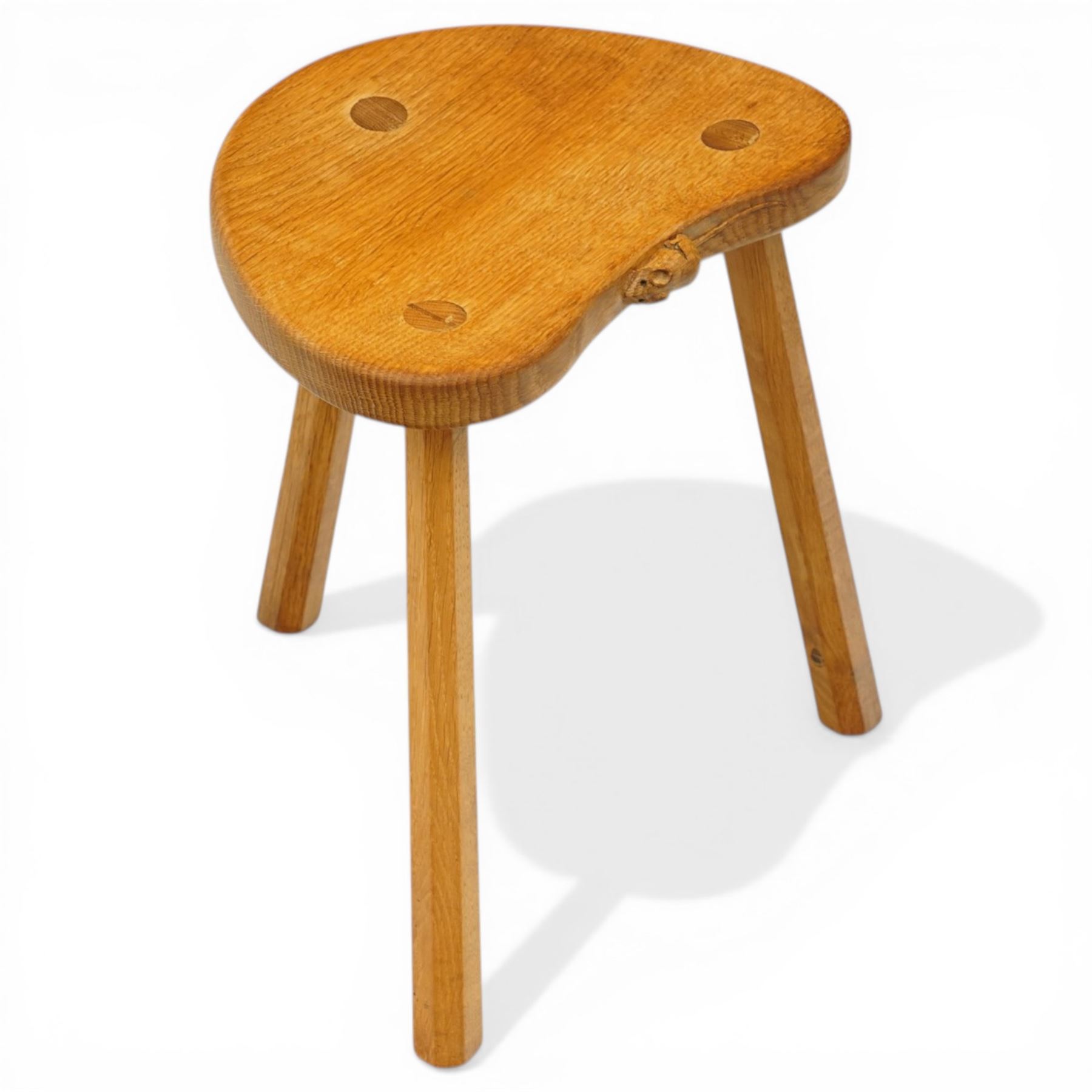 Mouseman - oak three-legged stool, dished kidney-shaped seat, raised on three octagonal splayed supports, with carved mouse signature, by the workshop of Robert Thompson of Kilburn